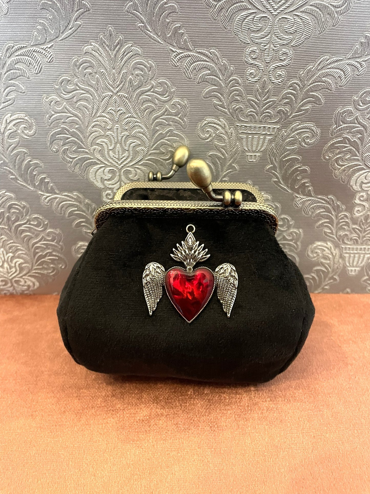 Détail du bijou baroque cœur sacré ailé en émail rouge et métal argenté ciselé.