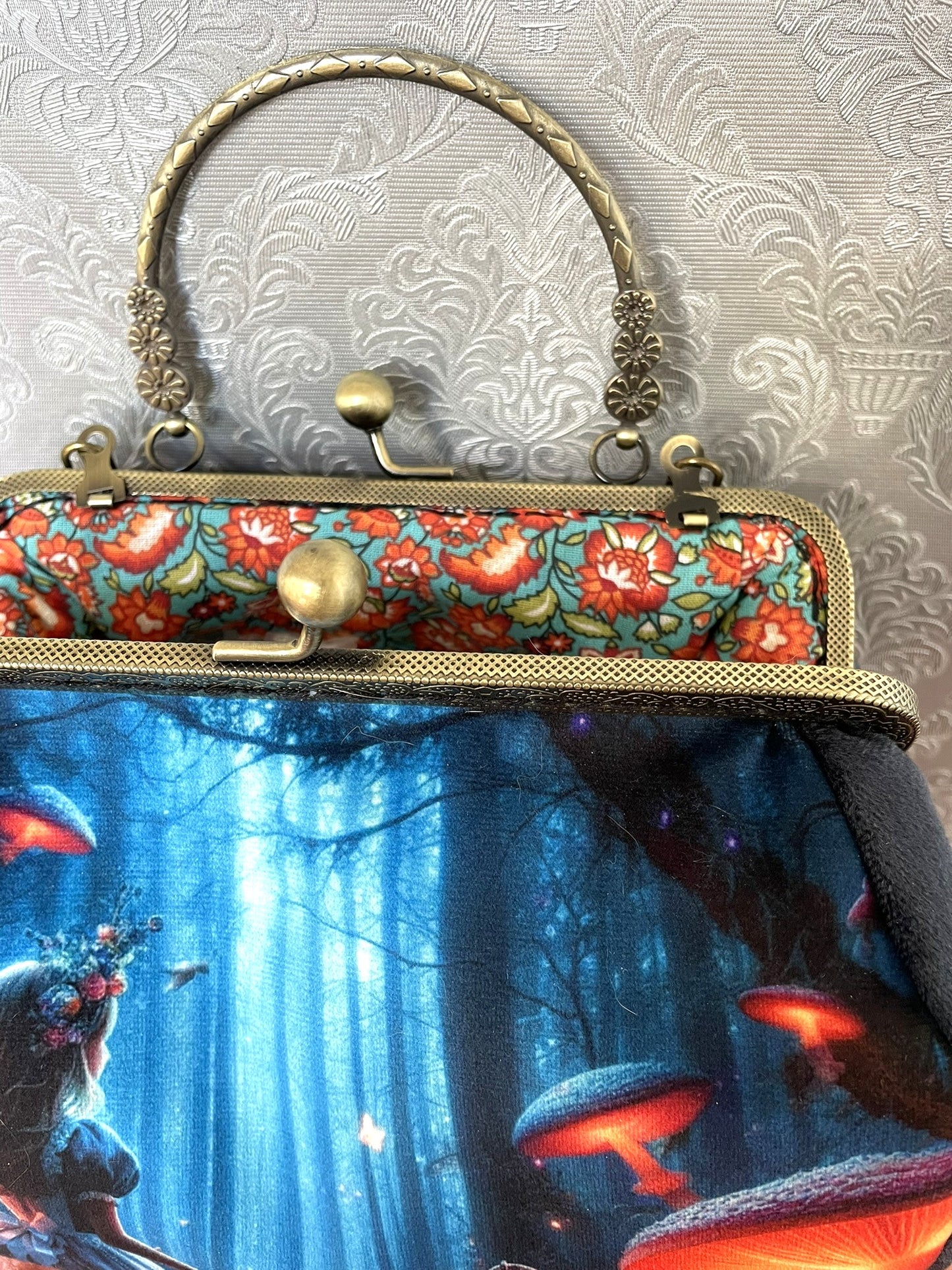 Détail du fermoir bronze vieilli et de la poignée rigide ciselée révélant une doublure en coton aux motifs floraux colorés.
