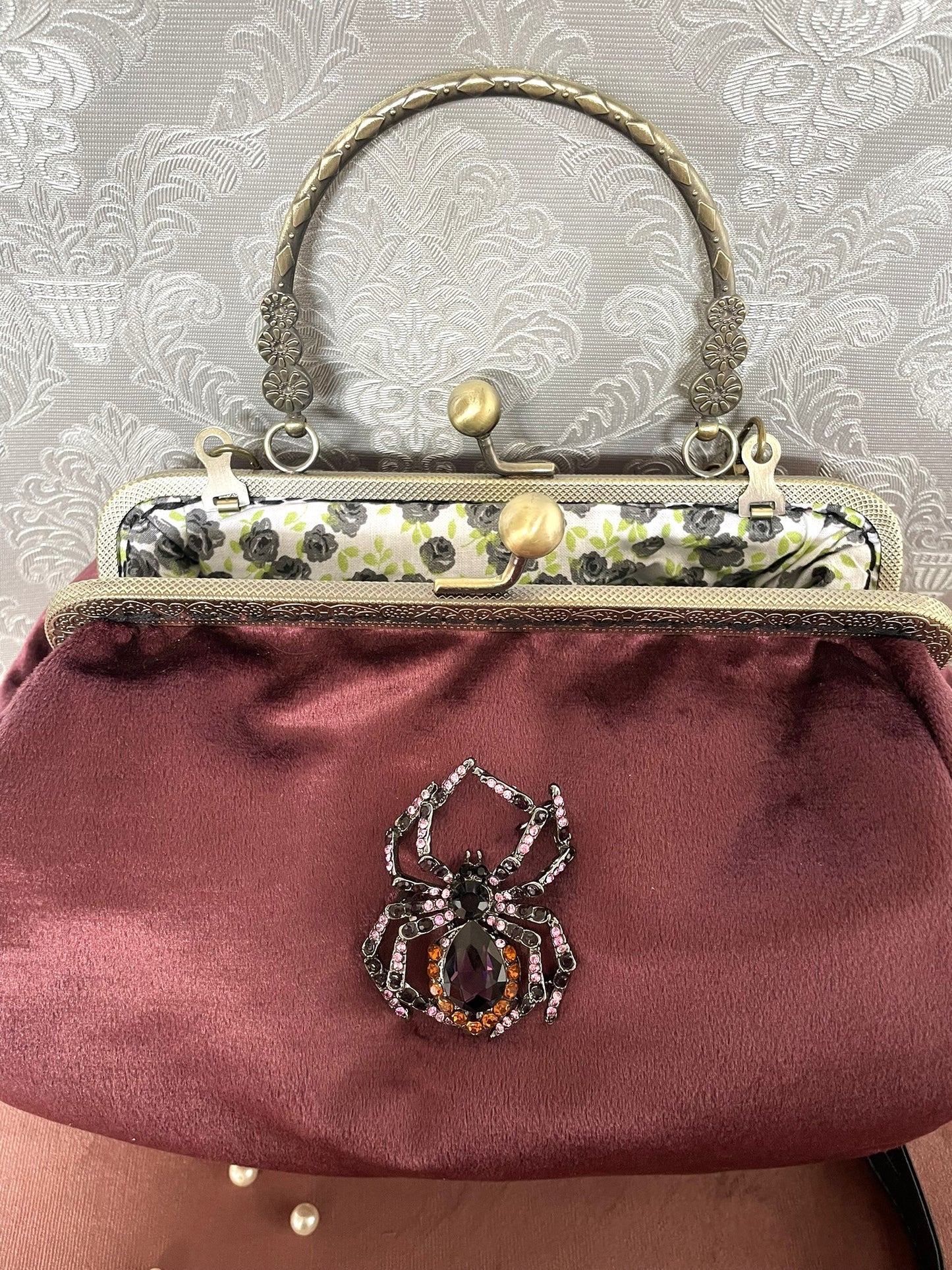 Détail d'un sac à main rétro bordeaux orné d'une broche araignée sertie de strass avec doublure fleurie.