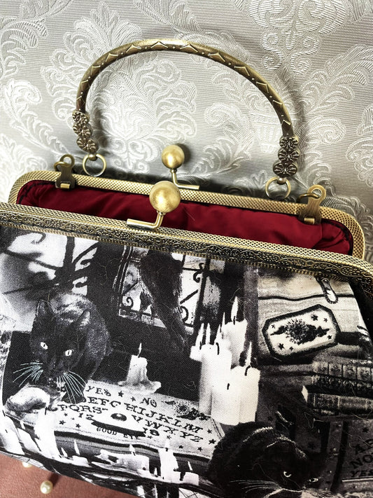 Détail d'un sac à main rétro illustrant un chat noir devant une planche Ouija et des bougies, avec doublure rouge bordeaux.