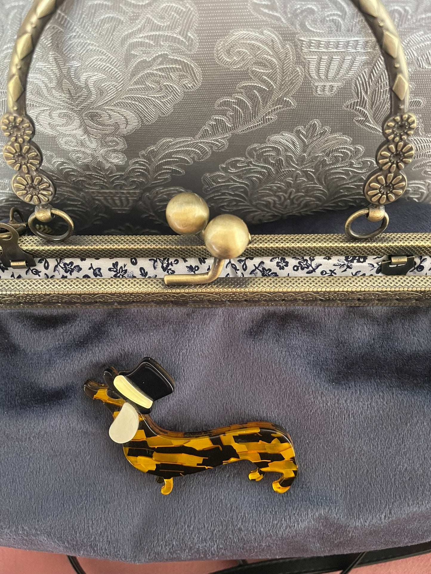 Zoom sur la broche teckel à haut-de-forme et la doublure en coton motif floral bleu et blanc d'un sac rétro.