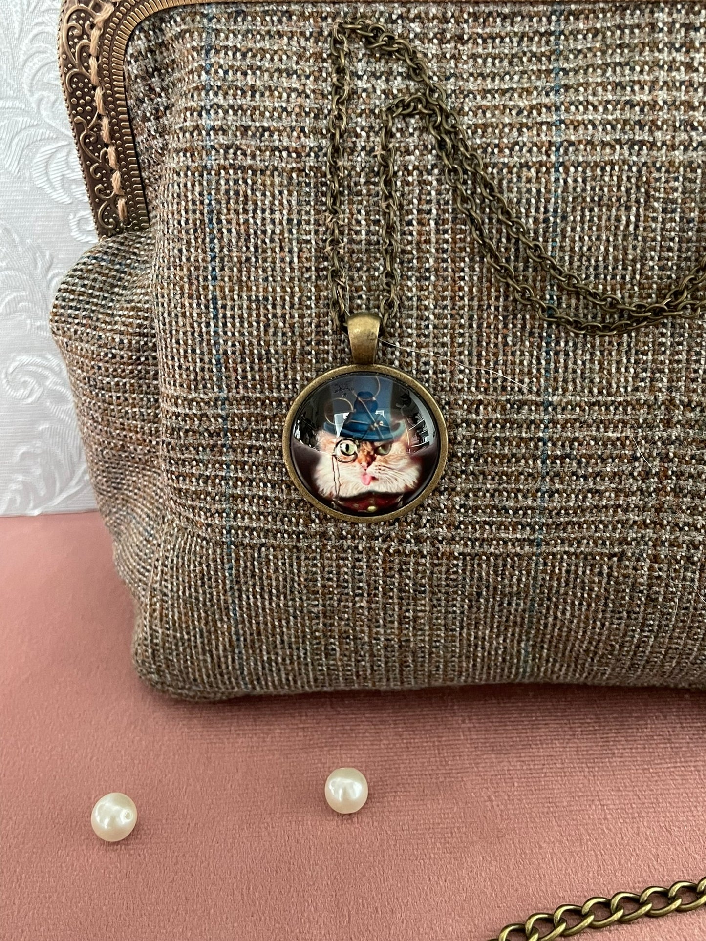 Gros plan sur le médaillon rétro représentant un chat détective à monocle et chapeau haut de forme bleu sur tissu tweed.