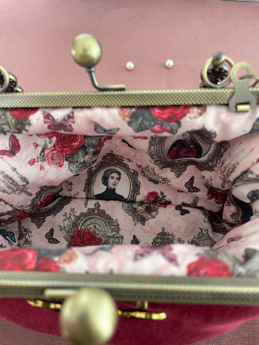 Vue intérieure de la pochette ouverte révélant une magnifique doublure victorienne rose avec portraits en camée, roses rouges, papillons