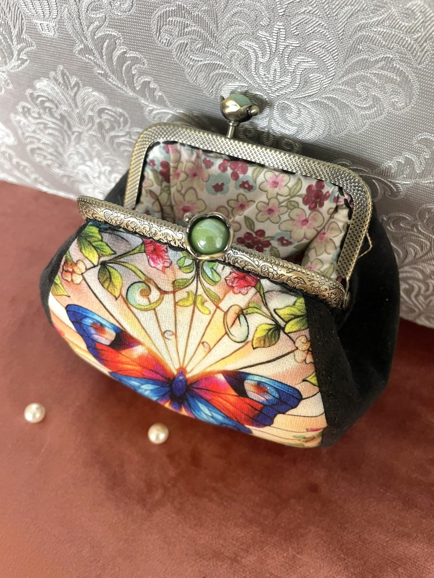 Vue intérieure du porte-monnaie montrant la doublure fleurie délicate et le cadre métallique rétro avec le fermoir orné d'une perle verte.