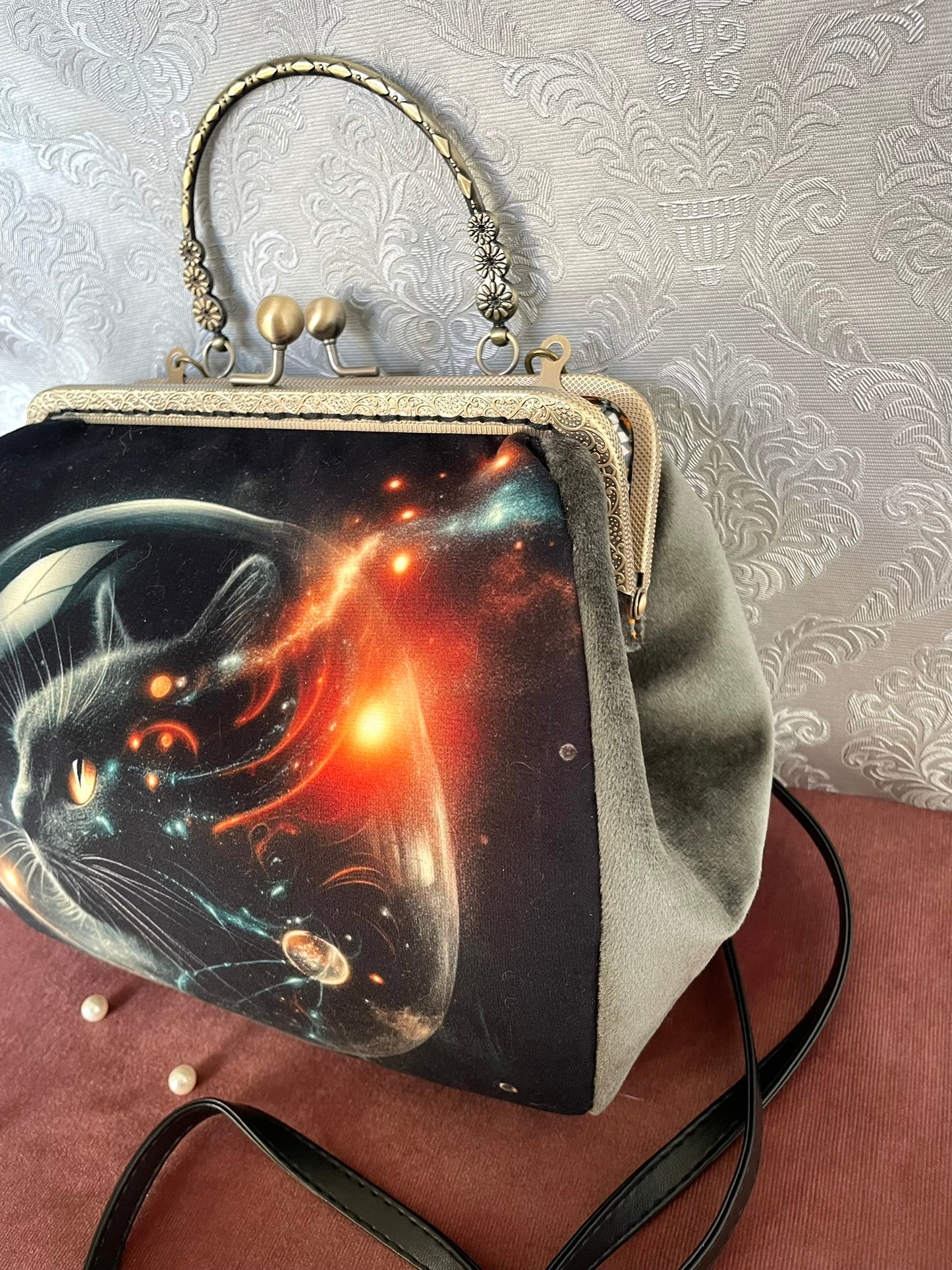 "Détail de profil d'un sac à main rétro en velours vert sauge illustrant un chat cosmique dans l'espace avec fermoir bronze antique