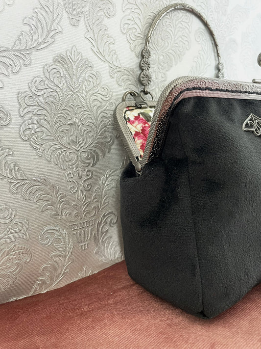 Détail de profil d'un sac à main artisanal en velours noir de qualité avec armature métallique rétro ciselée.