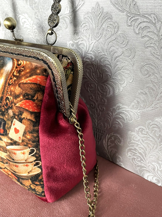 Gros plan latéral d'une pochette clutch féerique en velours bordeaux avec motif imprimé Alice au Pays des Merveilles et chaîne.