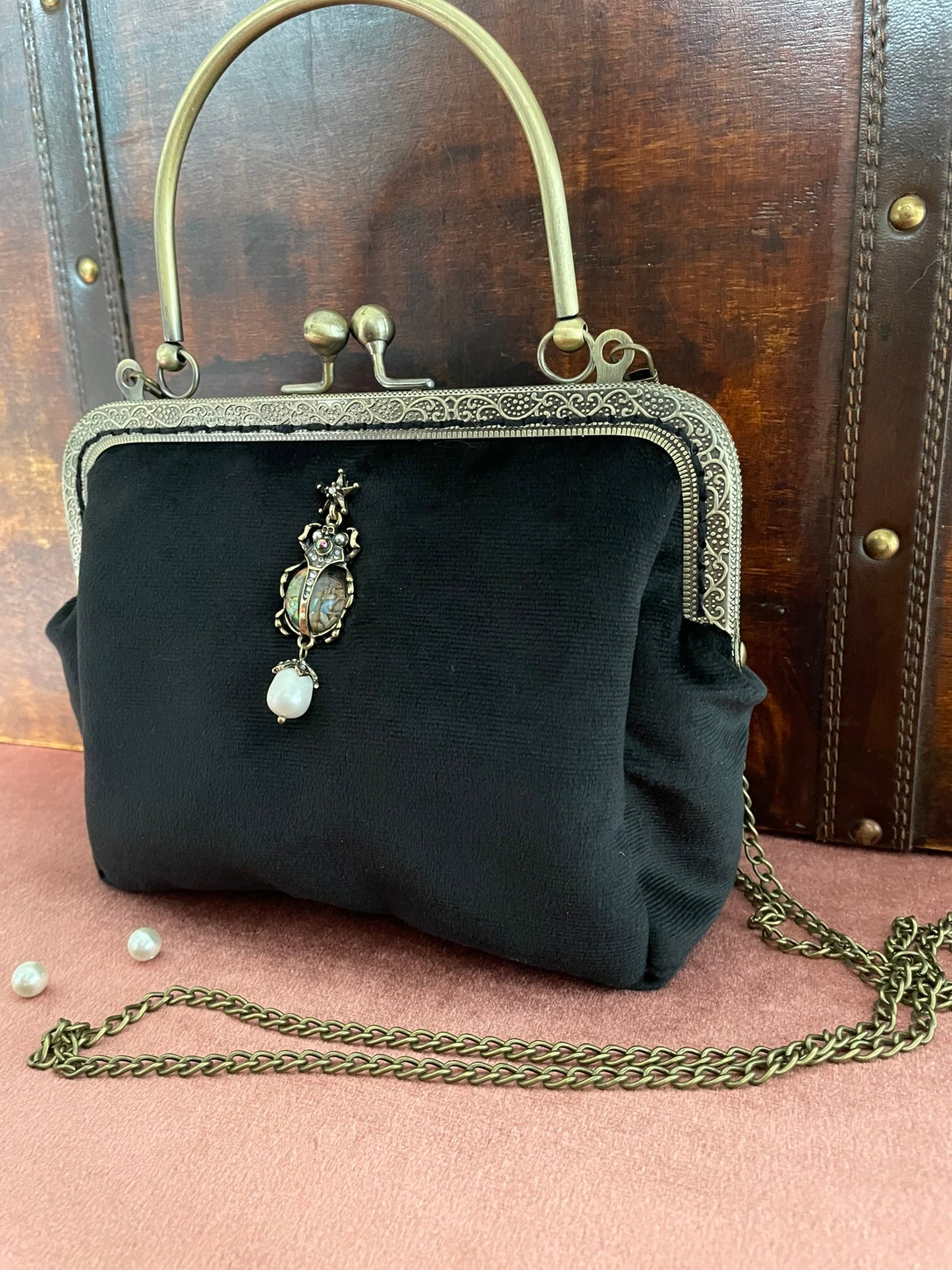 Vue de trois-quarts du sac rétro en velours noir montrant le fermoir cliquet et la bandoulière chaîne.