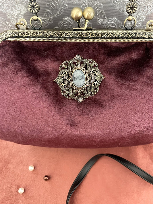 Détail de la broche camée de style antique entourée de strass sur velours bordeaux.