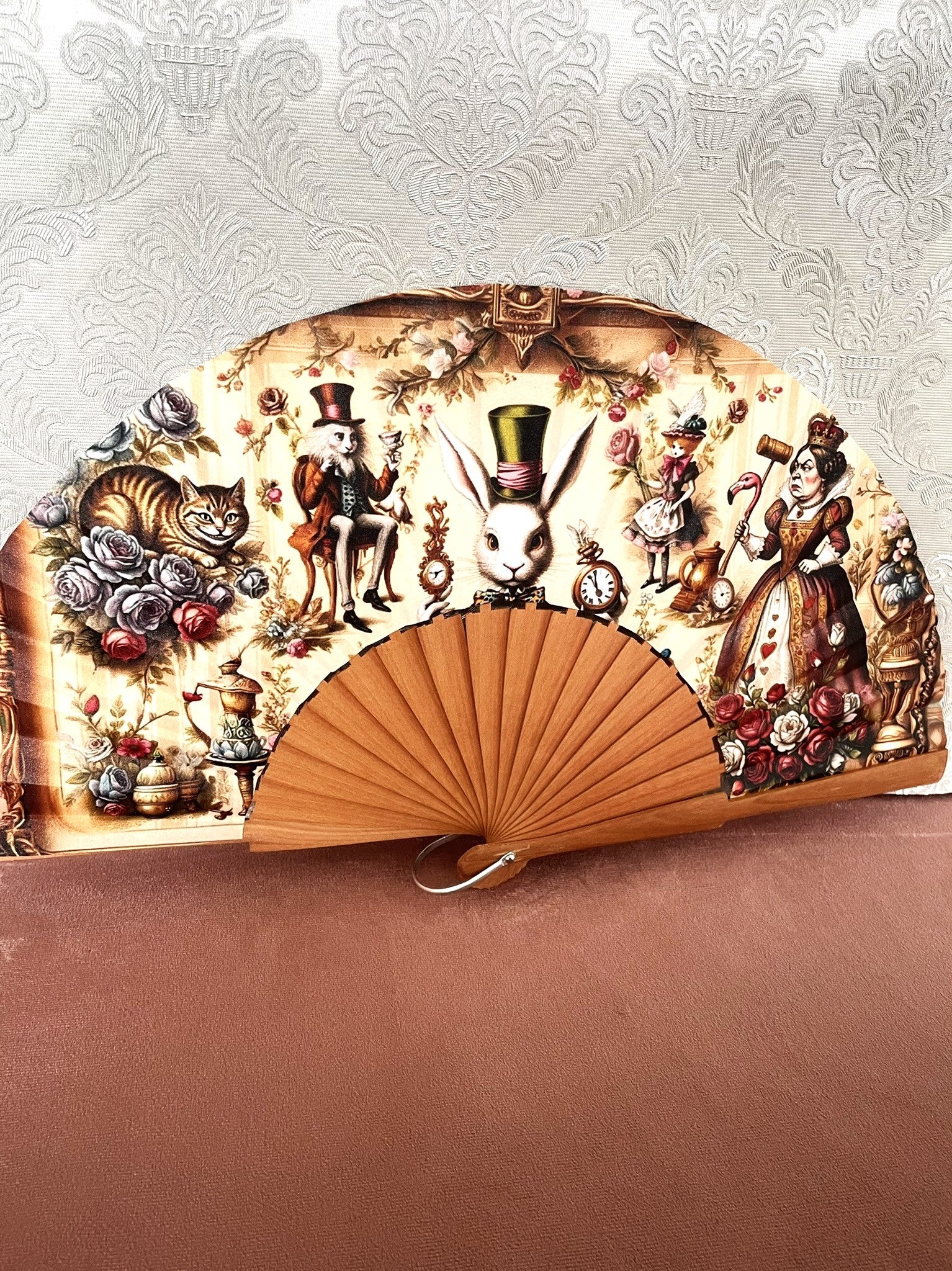 Détail du tissu exclusif d'un éventail en bois montrant les illustrations vintages d'Alice, du Lapin Blanc, du Chapelier Fou et de la Reine de Coeur parmi des roses.