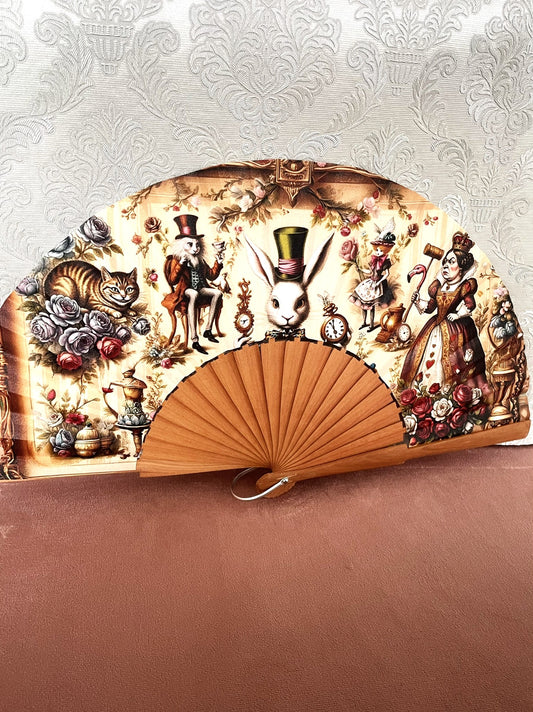 Détail du tissu exclusif d'un éventail en bois montrant les illustrations vintages d'Alice, du Lapin Blanc, du Chapelier Fou et de la Reine de Coeur parmi des roses.