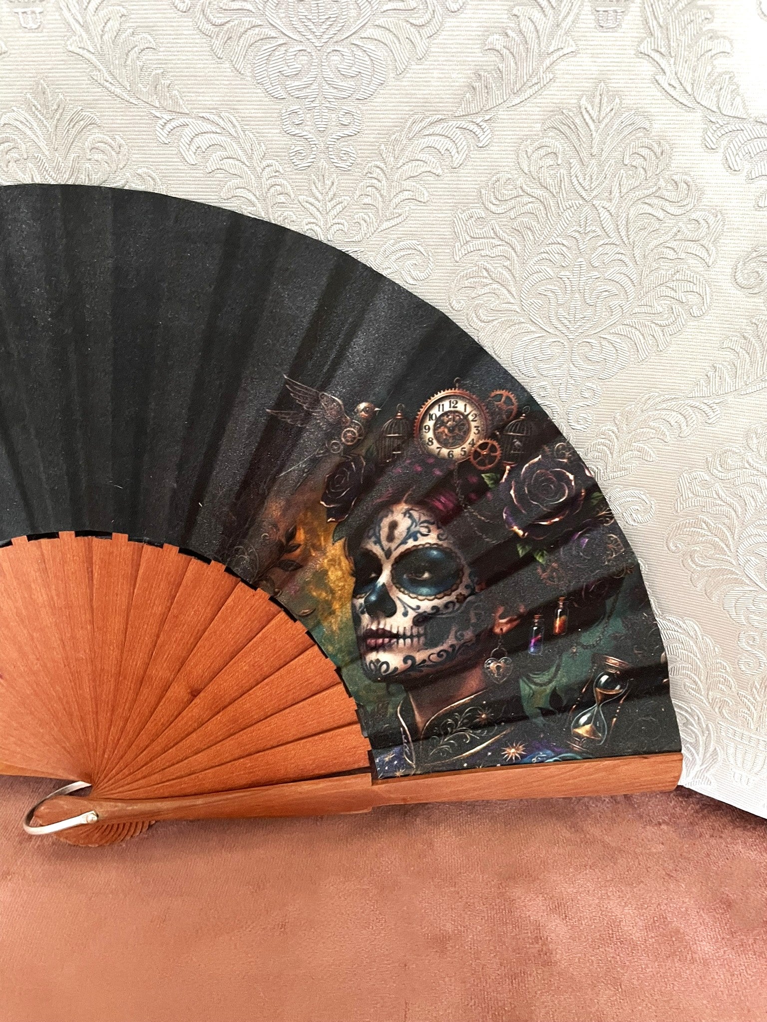 Gros plan sur l'illustration d'une Catrina steampunk avec des engrenages, une horloge et des roses sombres sur le tissu d'un éventail en bois de fruitier.