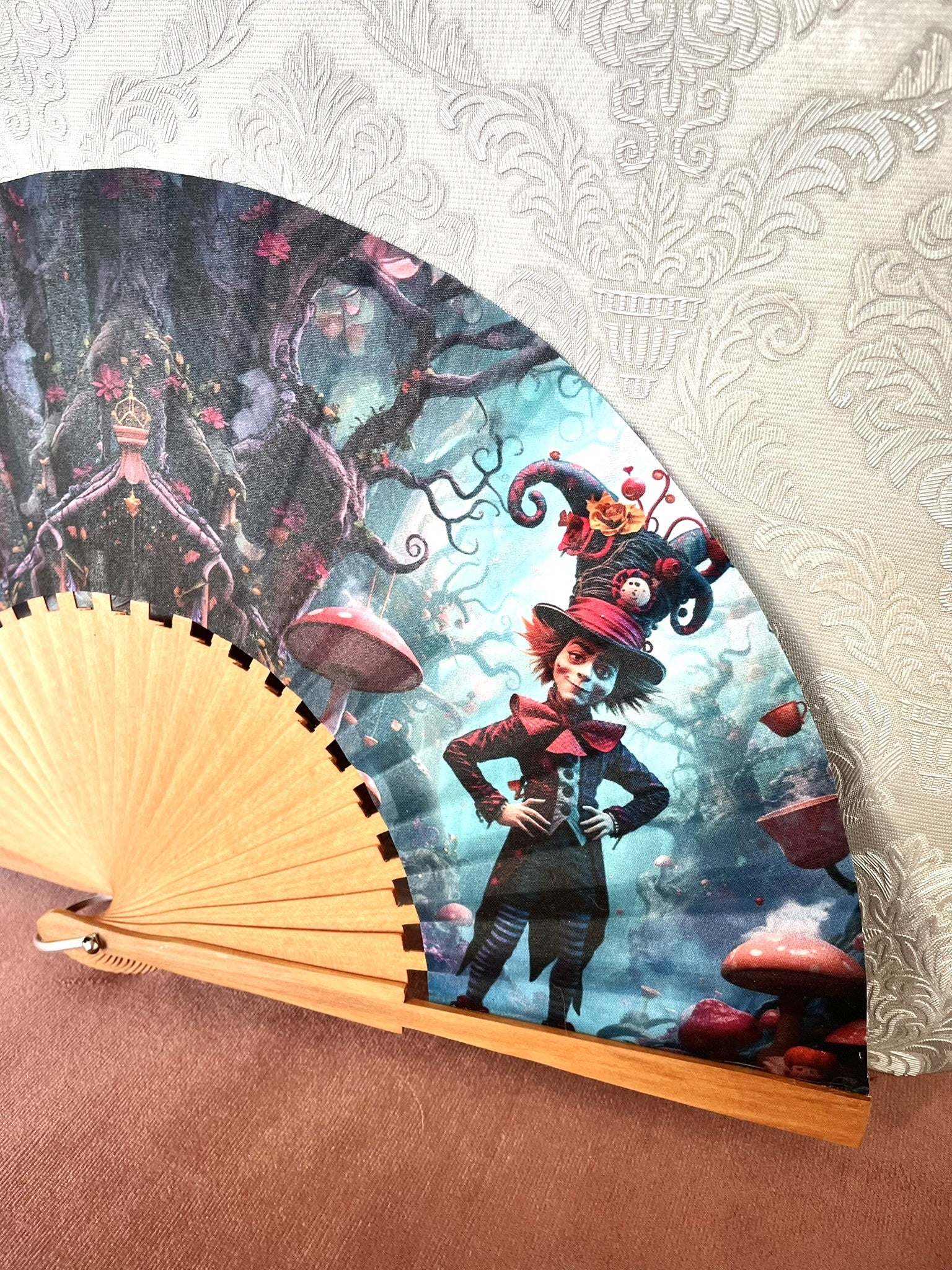 Détail du tissu exclusif d'un éventail en bois montrant le personnage du Chapelier Fou coiffé de son haut-de-forme fantaisie dans un décor féerique.