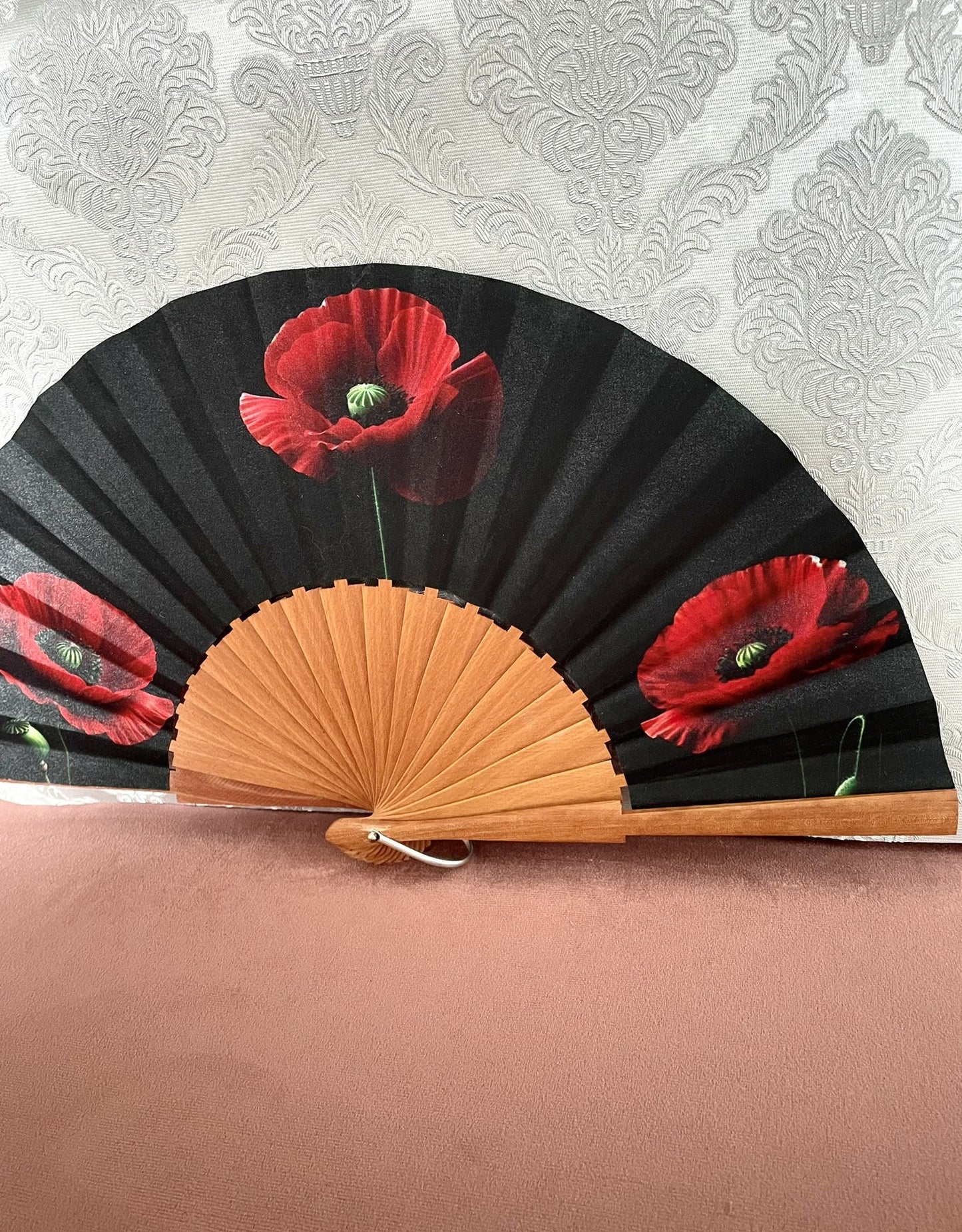 Détail du tissu exclusif d'un éventail en bois montrant des fleurs de coquelicot rouge vif sur un fond noir intense.