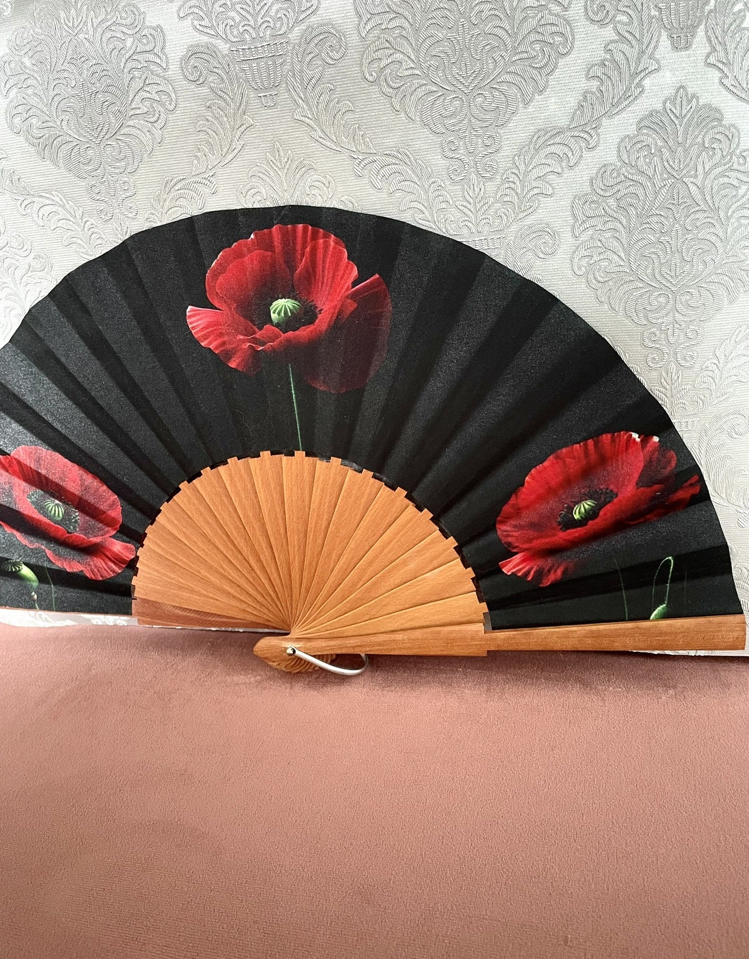 Détail du tissu exclusif d'un éventail en bois montrant des fleurs de coquelicot rouge vif sur un fond noir intense.