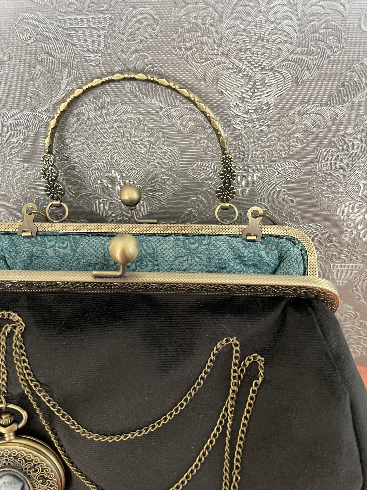 Intérieur ouvert du sac noir révélant une doublure bleu émeraude aux motifs baroques.