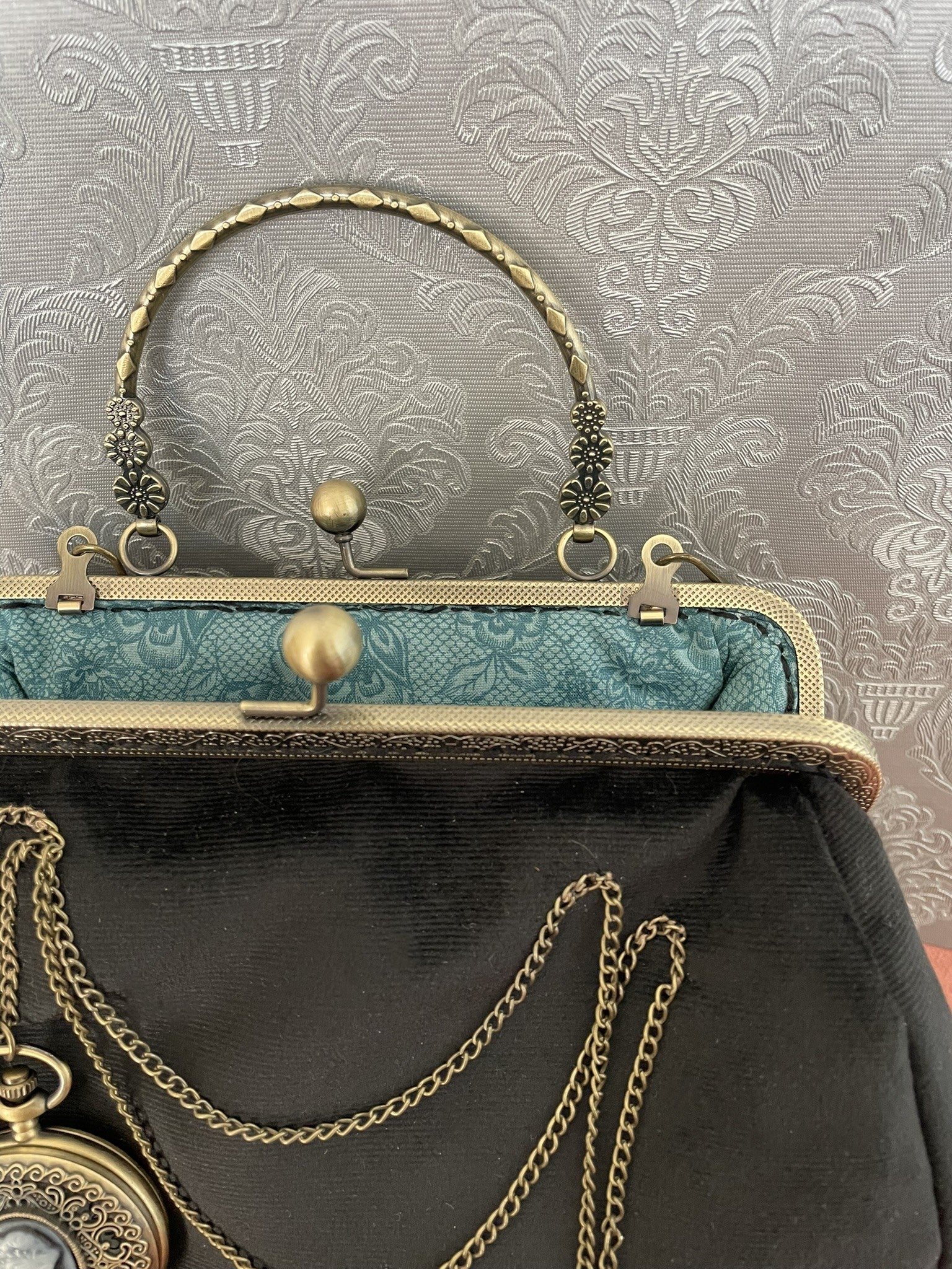 Intérieur ouvert du sac noir révélant une doublure bleu émeraude aux motifs baroques.
