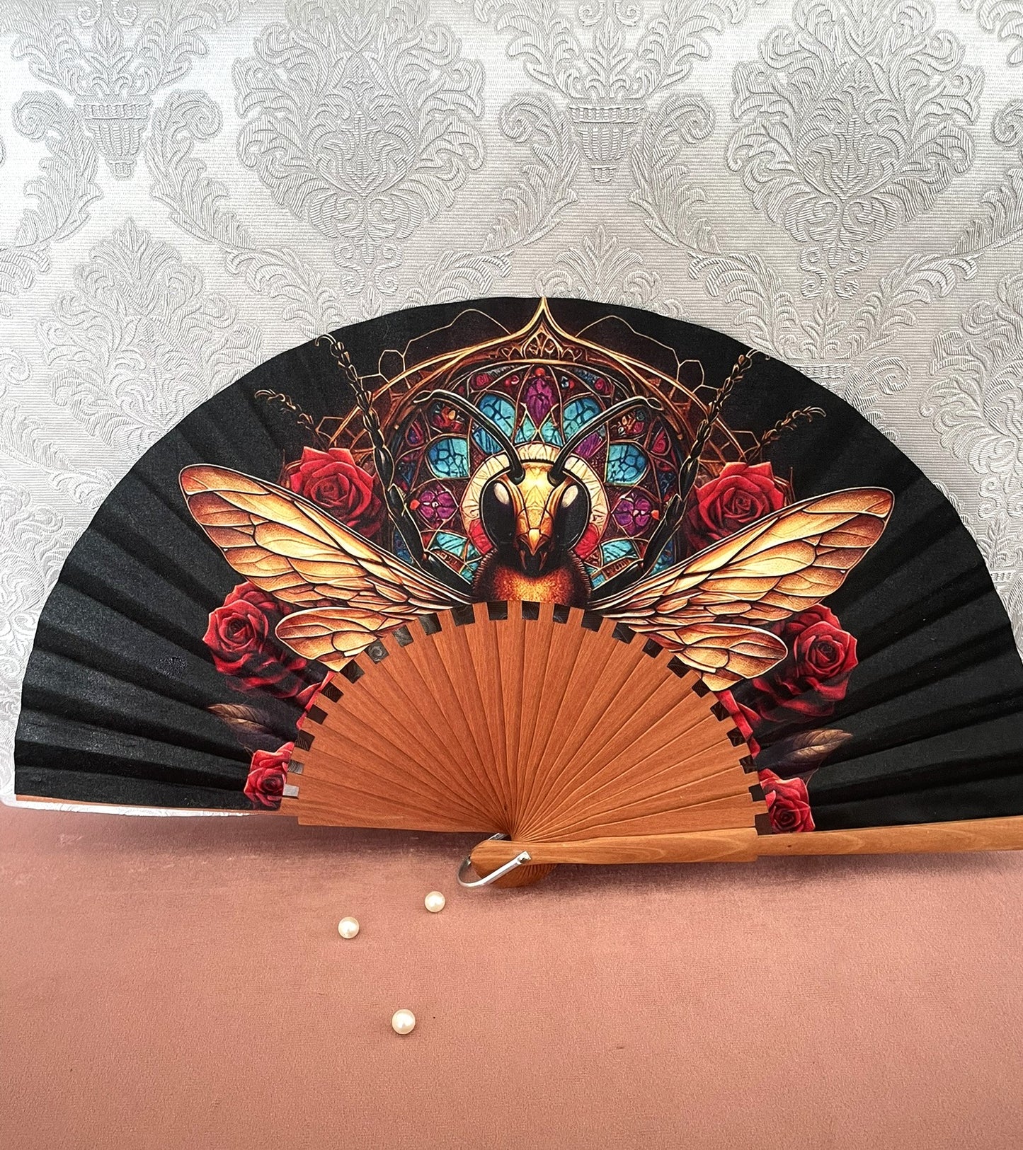 Éventail artisanal en bois fait main modèle abeille dorée devant un vitrail gothique et des roses rouges