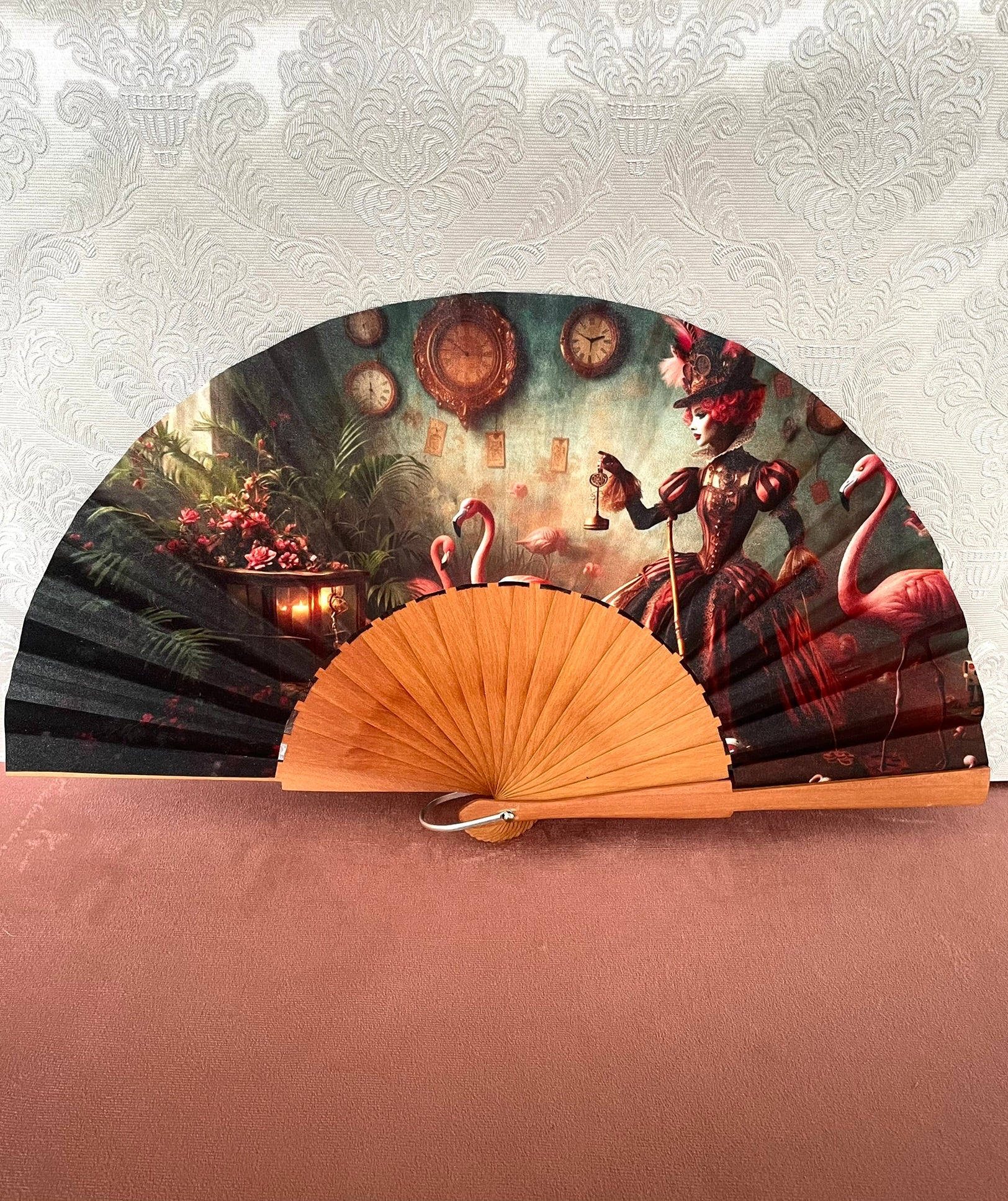Éventail artisanal ouvert Le Comptoir de Suzanne en bois avec tissu exclusif représentant la Reine de Cœur entourée de flamants roses et d'horloges vintage.