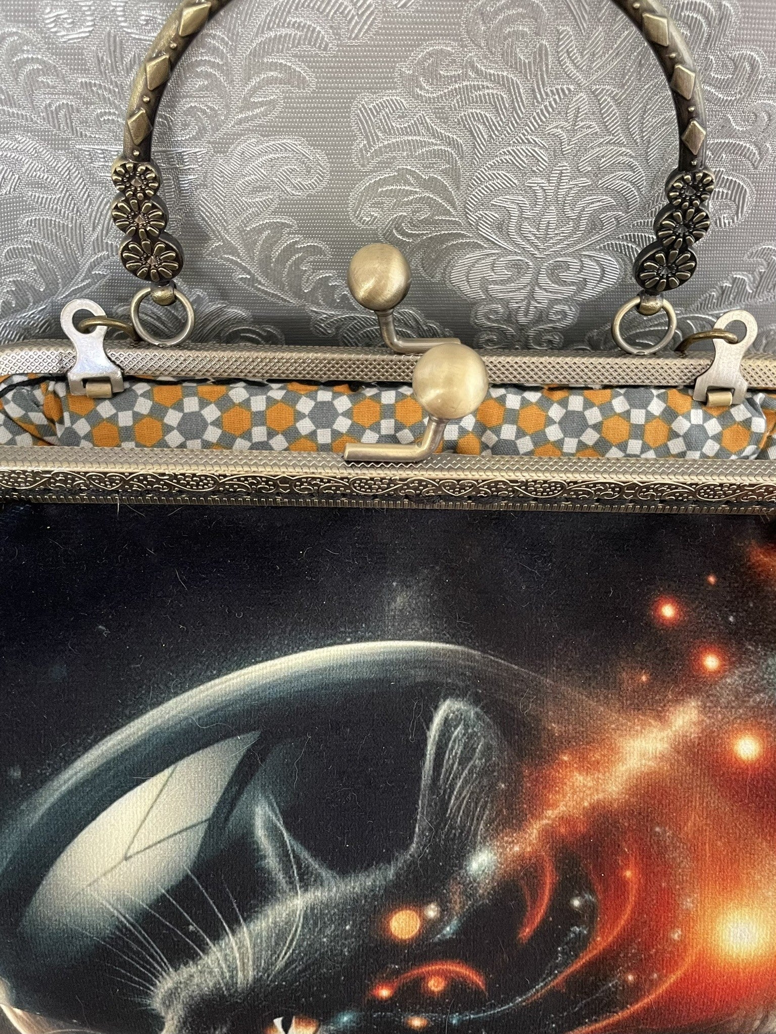 Zoom sur le fermoir cliquet en bronze ciselé et la doublure intérieure au motif géométrique rétro d'un sac sur le thème de l'espace.