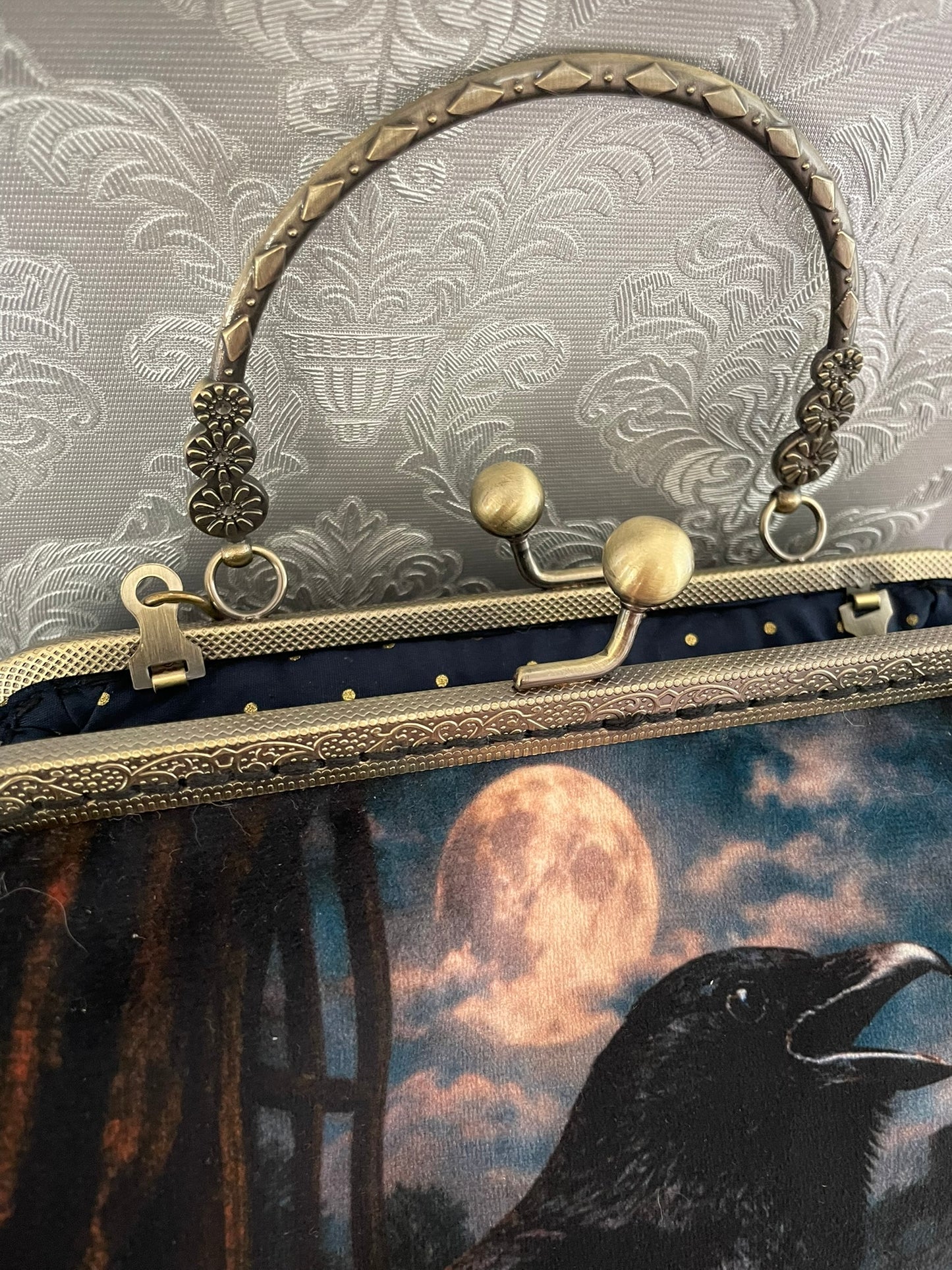 Zoom sur le fermoir cliquet en bronze antique et la doublure intérieure bleu nuit à pois dorés du sac corbeau