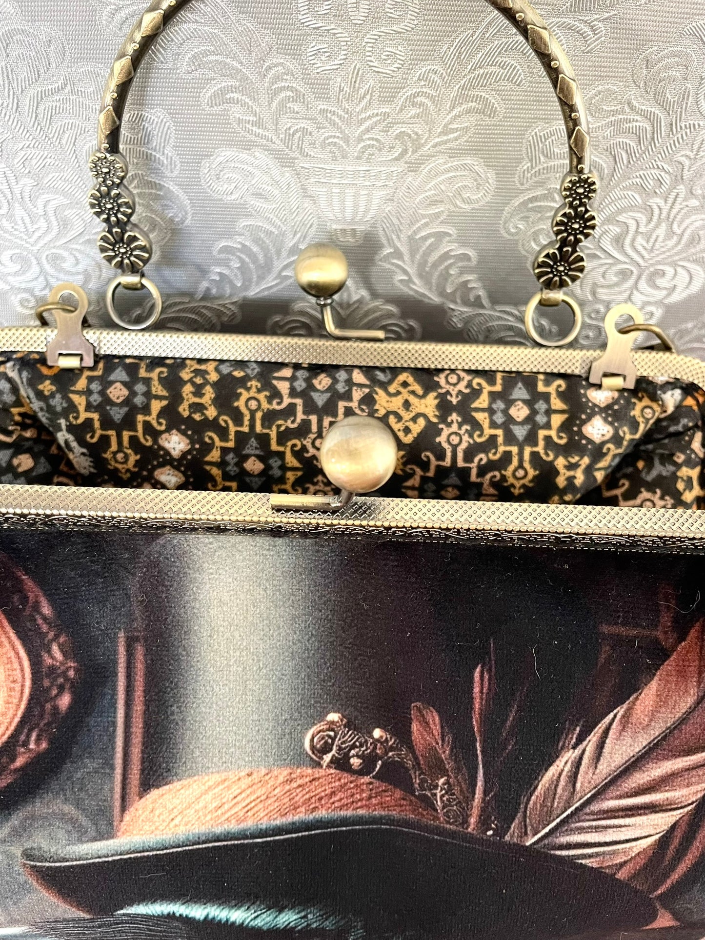 Zoom sur le fermoir clic-clac en bronze ciselé et la doublure intérieure au motif géométrique rétro d'un sac dandy victorien.