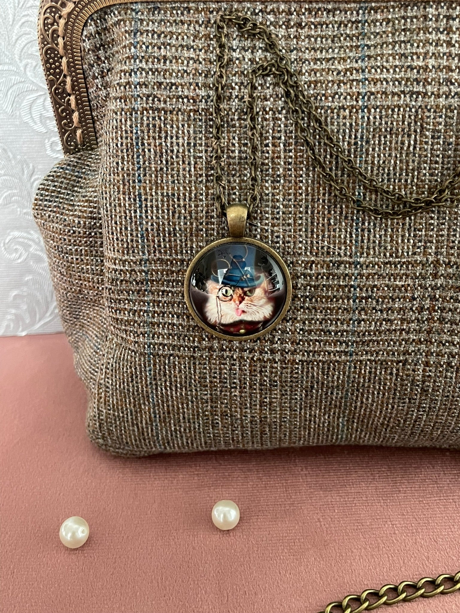 Gros plan sur le médaillon rétro représentant un chat détective à monocle et chapeau haut de forme bleu sur tissu tweed.