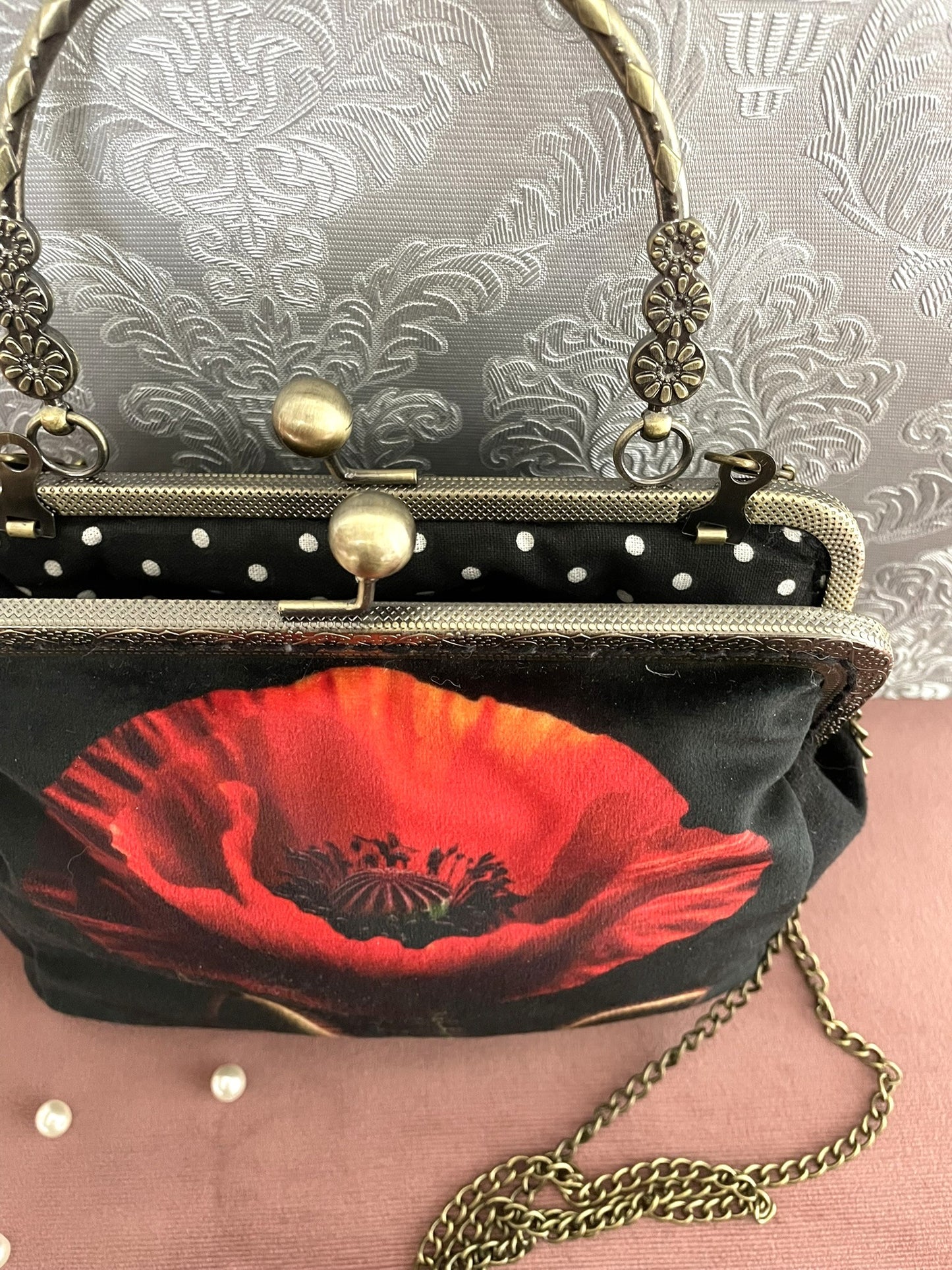 Vue du dessus de la pochette coquelicot rouge ouverte révélant le fermoir esprit vintage et sa doublure noire à petits pois blancs.