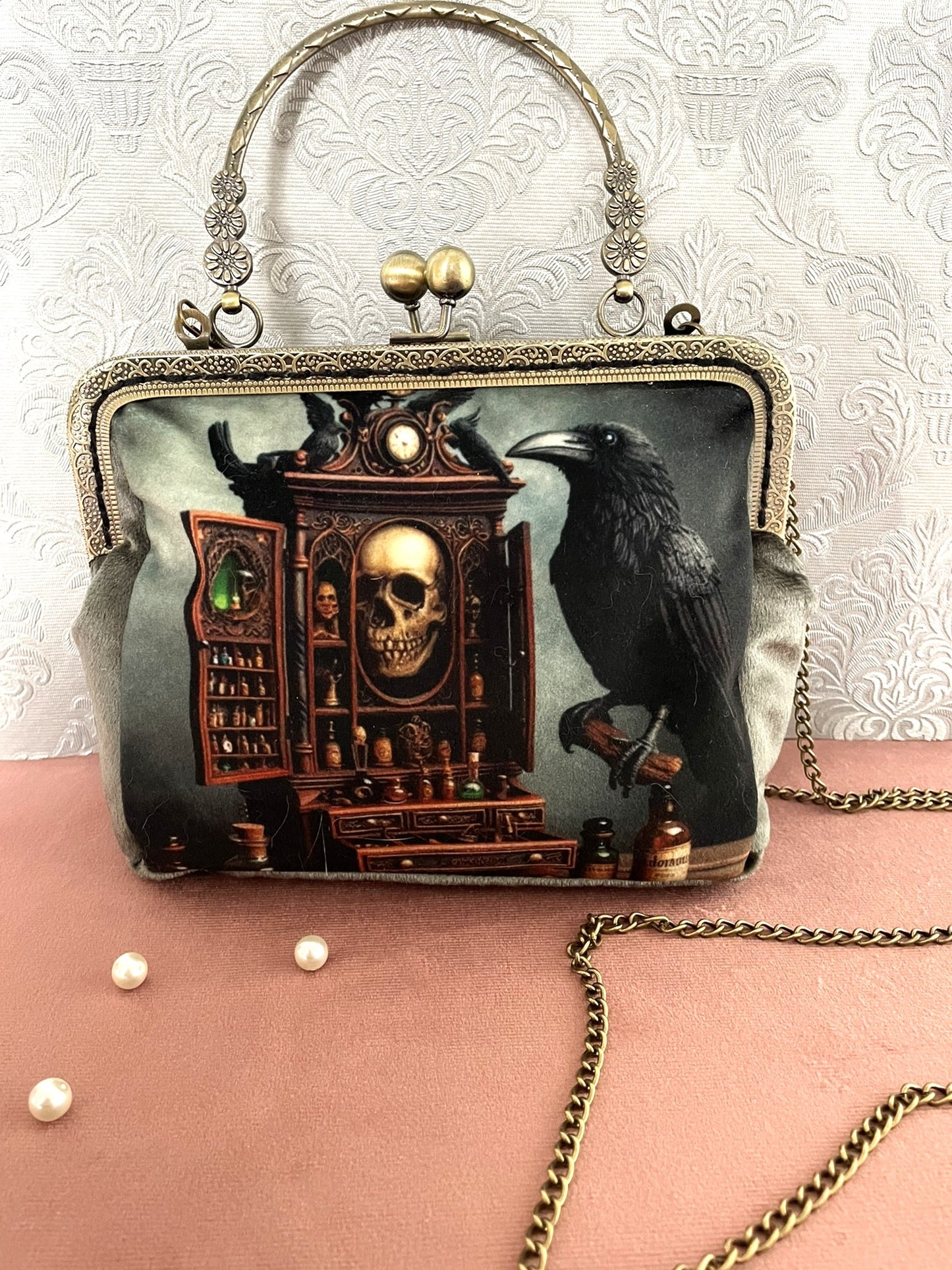 Pochette clutch gothique de face avec illustration de corbeau noir et meuble de sorcellerie avec crâne, poignée ciselée et chaîne.