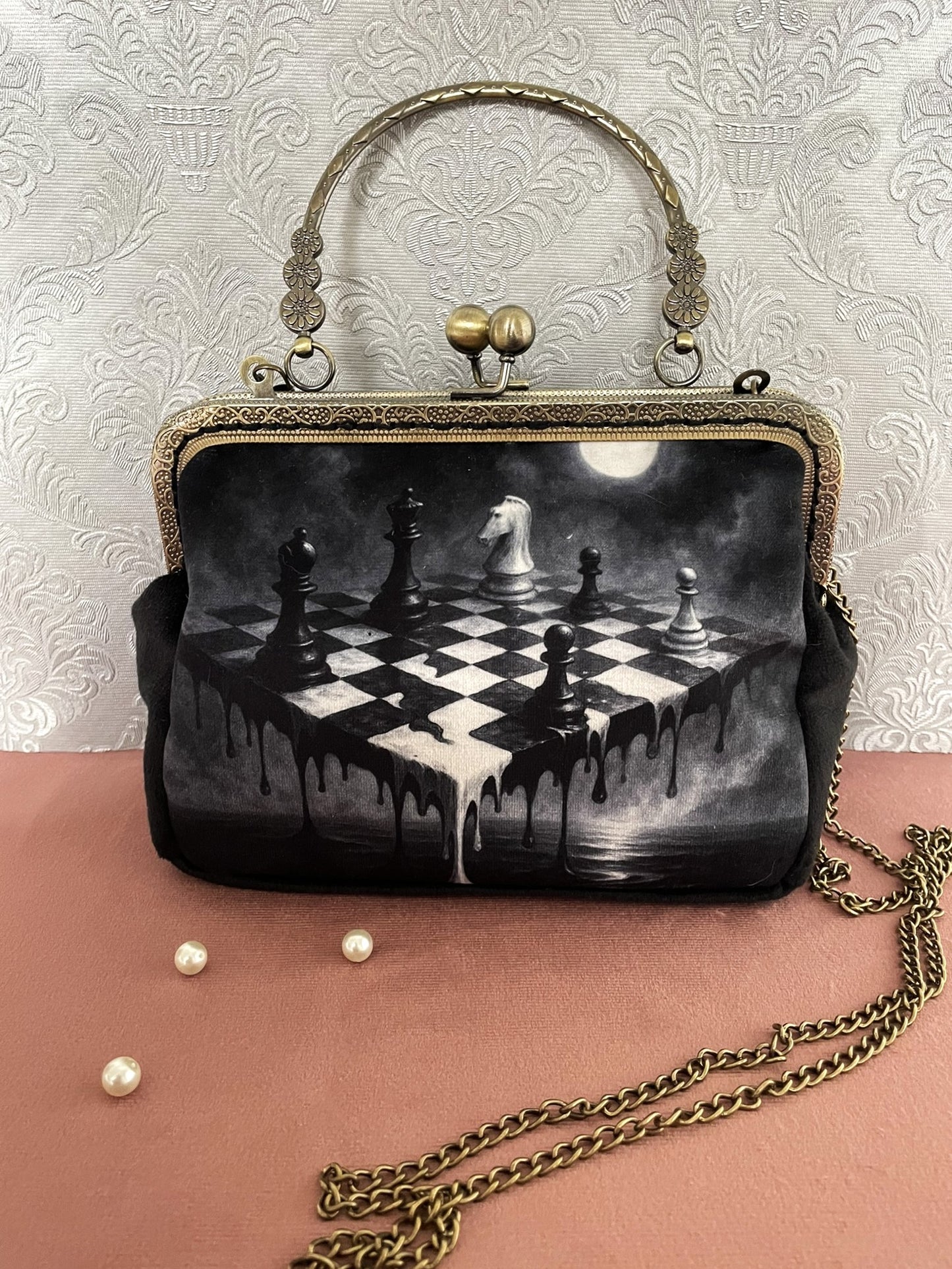 Pochette clutch gothique de face avec illustration d'un échiquier surréaliste en noir et blanc sous la lune, poignée métallique ciselée et chaîne .