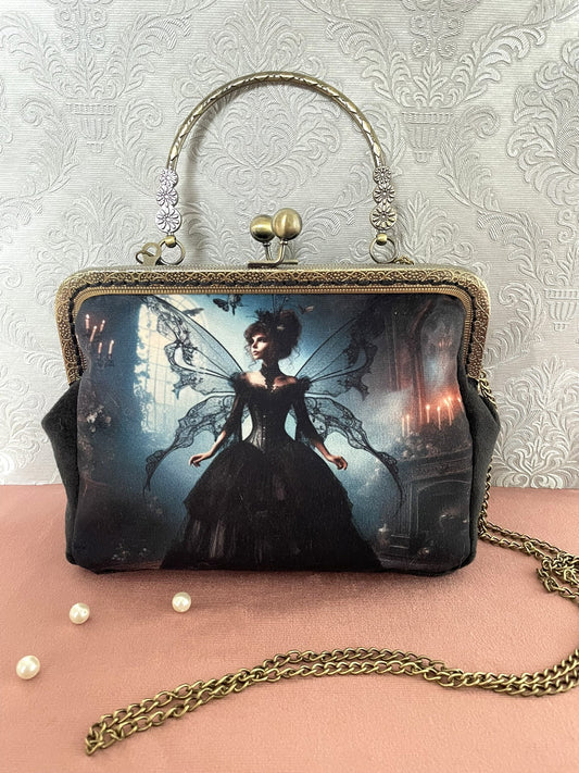 Pochette clutch de face représentant une fée gothique en robe noire avec de grandes ailes, poignée rigide bronze et chaîne bandoulière.