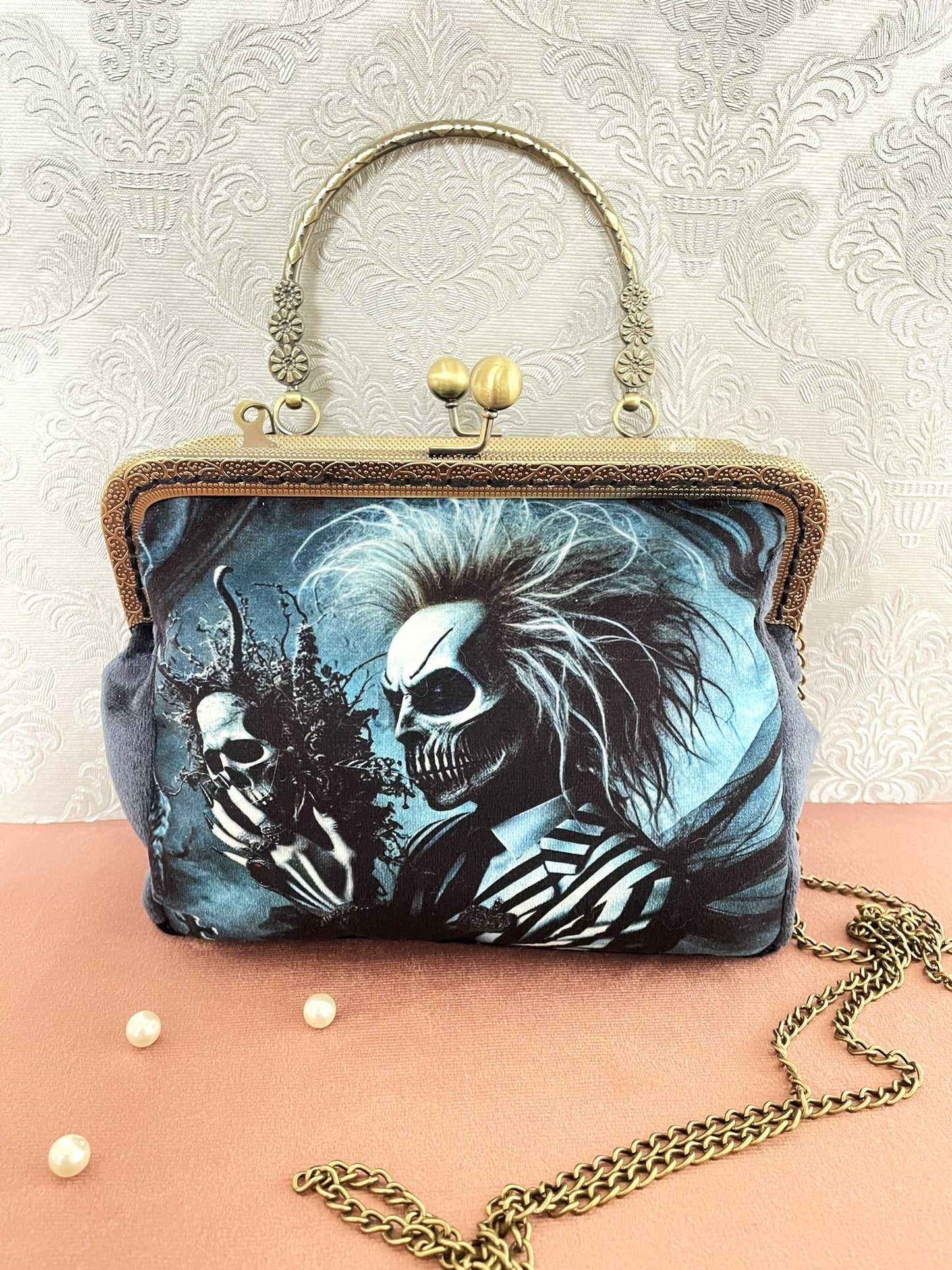 Vue de face de la pochette clutch gothique en velours bleu représentant un personnage squelette au costume rayé fantastique avec sa chaîne amovible.