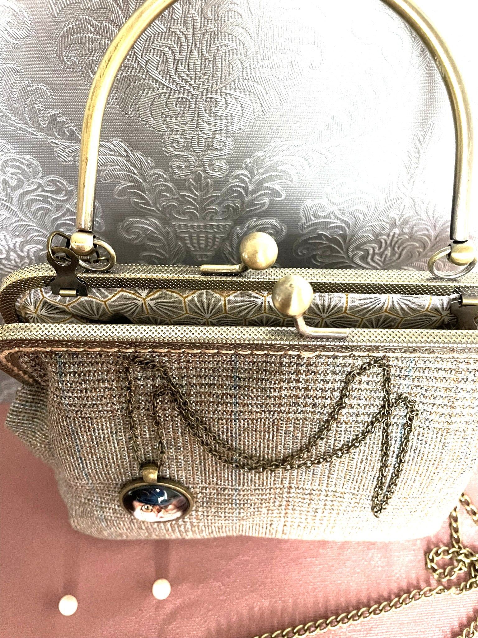 Pochette clutch vintage en tweed ouverte dévoilant une doublure graphique grise et dorée,  fermoir style rétro et médaillon chat steampunk.