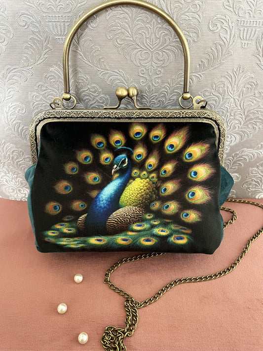Pochette clutch de face en velours représentant un paon majestueux faisant la roue, avec poignée rigide bronze et chaîne.