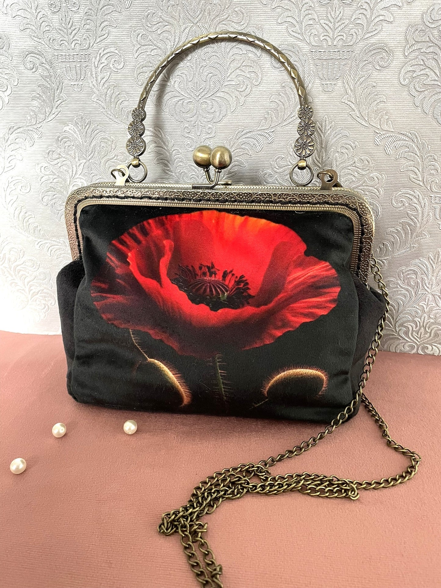 Pochette clutch de face en velours noir avec un gros plan artistique d'un coquelicot rouge vif, poignée ciselée bronze et chaîne
