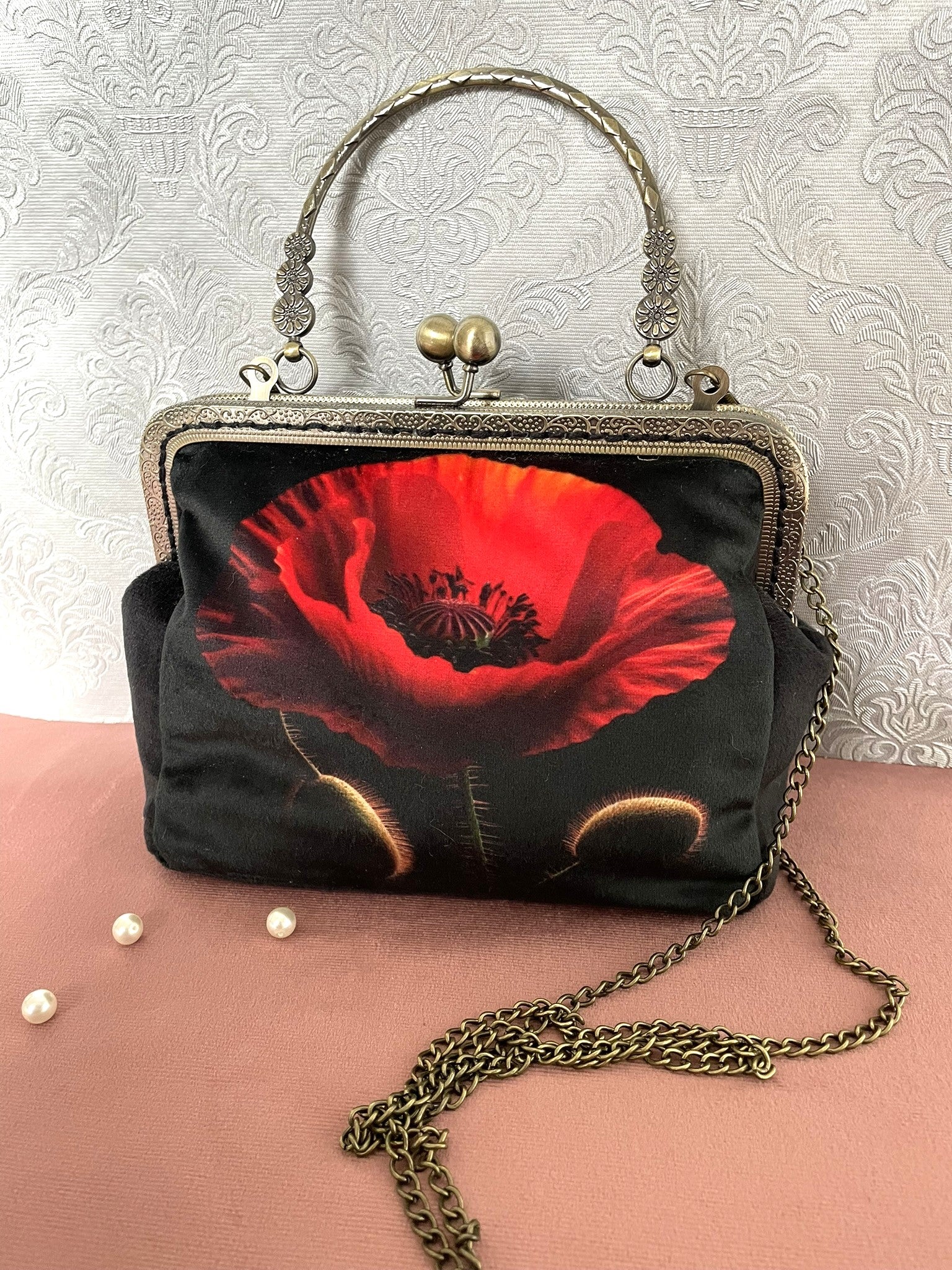 Pochette clutch de face en velours noir avec un gros plan artistique d'un coquelicot rouge vif, poignée ciselée bronze et chaîne