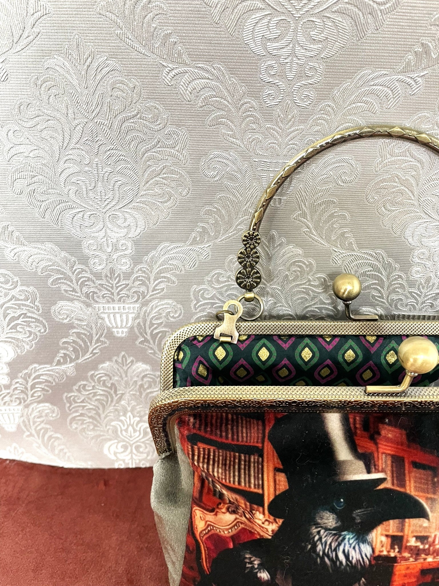 Pochette artisanale corbeau victorien, armature bronze et décor rouge.