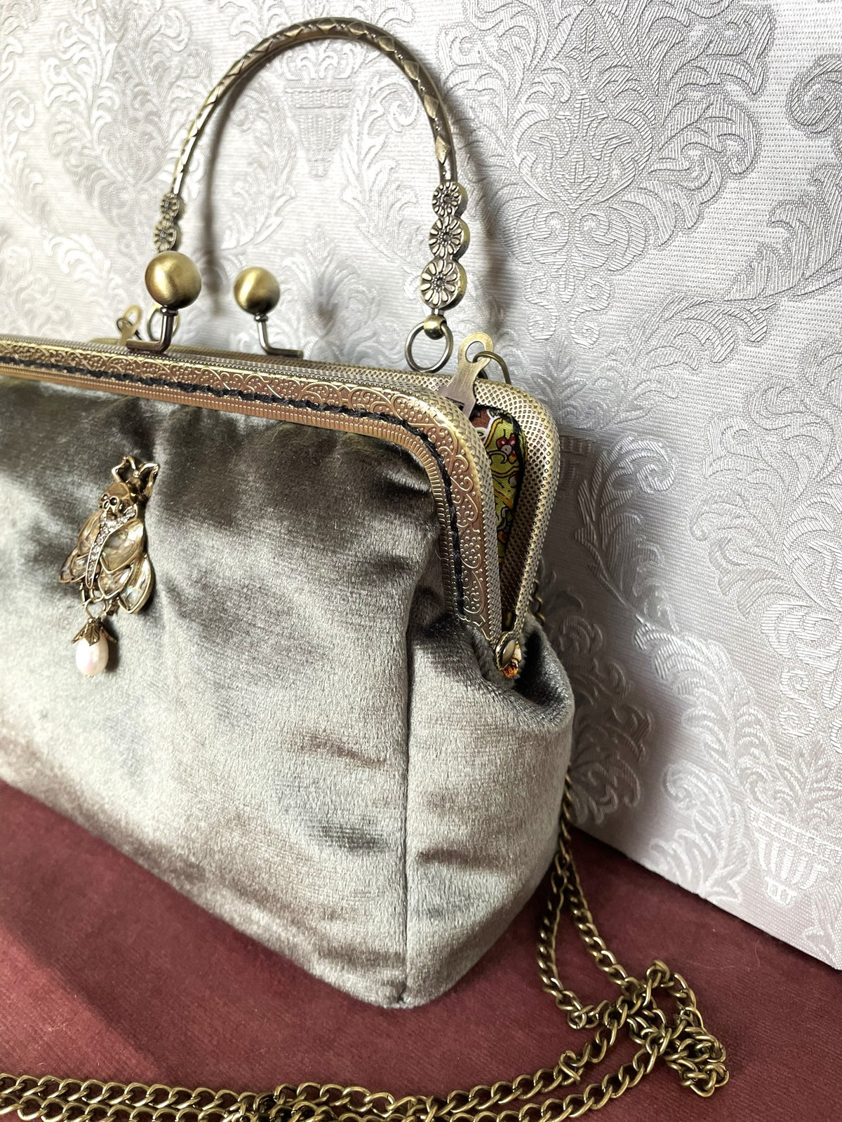 Vue de profil pochette rétro velours vert sauge avec bijou phalène tête de mort et chaînette couleur bronze Le Comptoir de Suzanne
