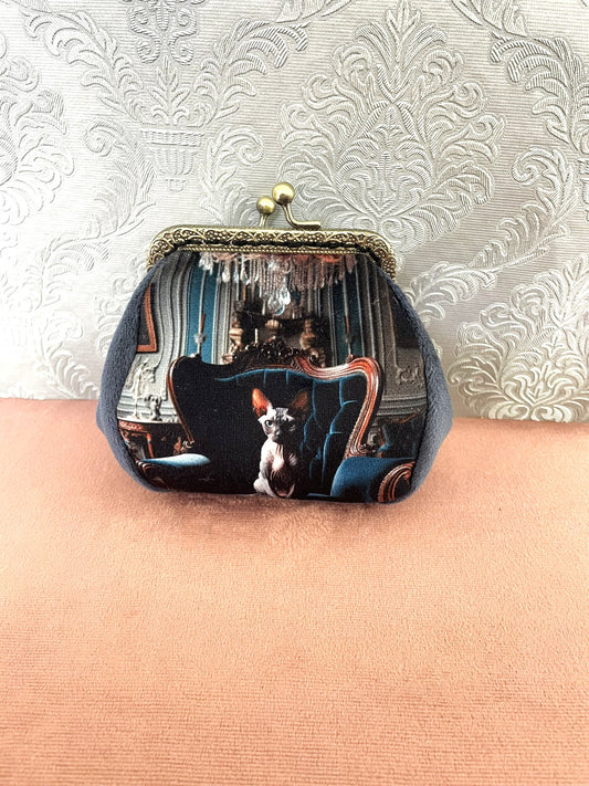 Porte-monnaie vintage fait main représentant un chat Sphynx assis sur un fauteuil baroque bleu sous un lustre en cristal.