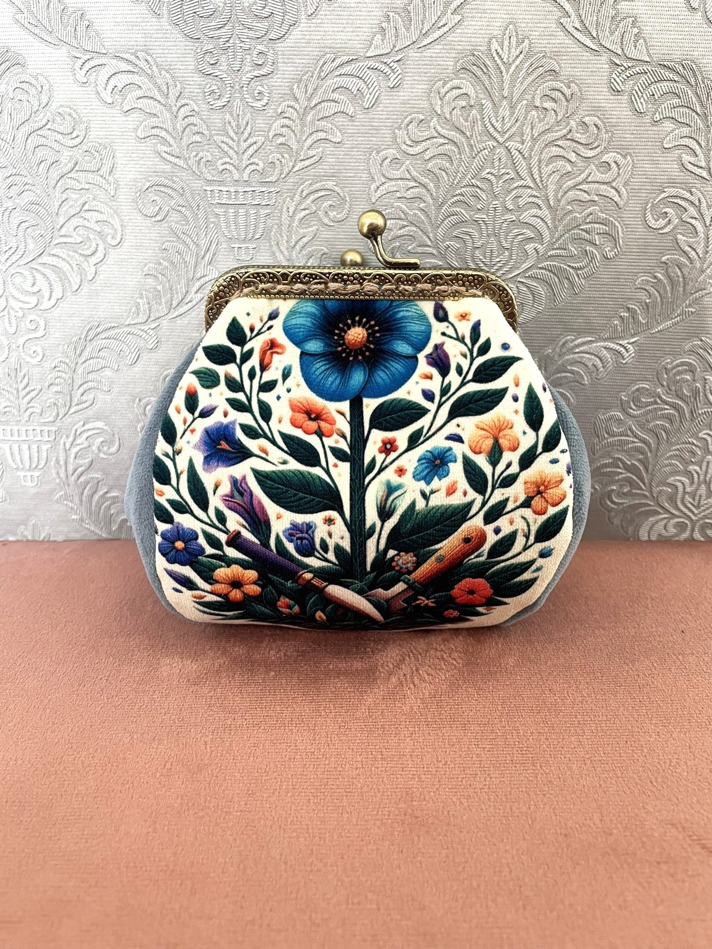 Porte-monnaie vintage fait main avec illustration de grande fleur bleue et outils de jardin botaniques rétro.