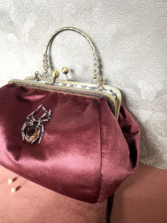 Vue de profil d'un sac à main rétro en velours bordeaux lie-de-vin avec fermoir cliquet effet bronze antique.
