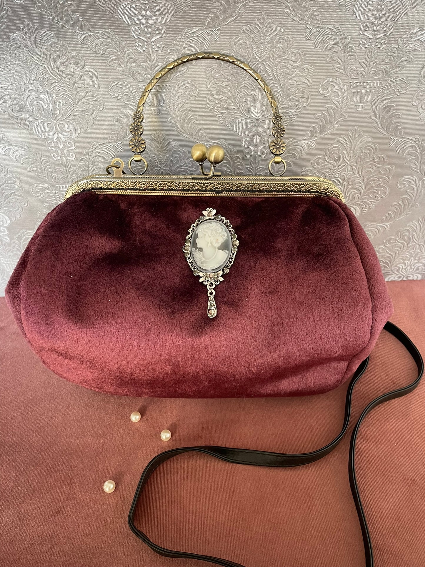 Détail de profil d'un sac à main rétro en velours bordeaux orné d'un camée victorien avec broche ciselée.