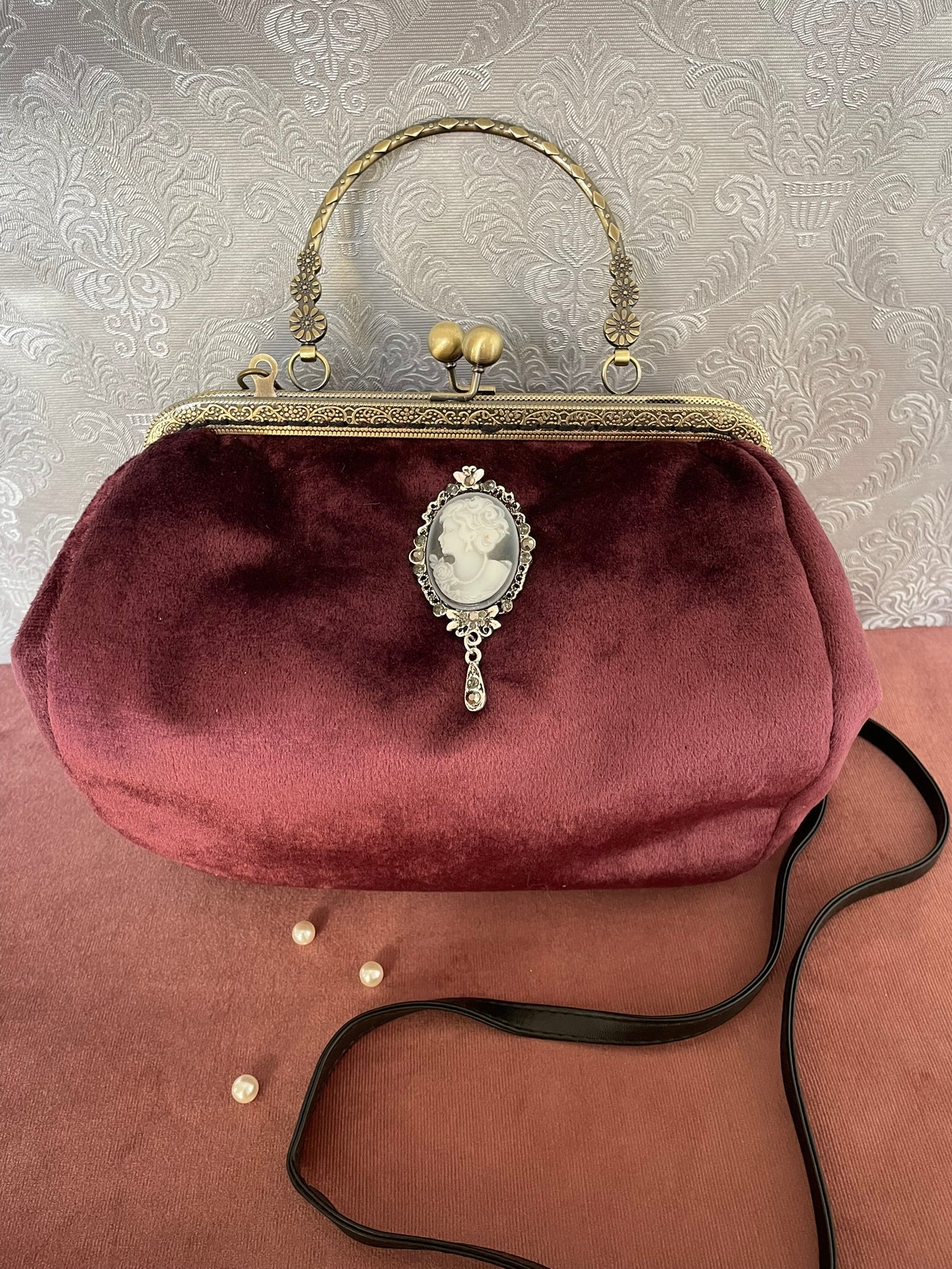 Détail de profil d'un sac à main rétro en velours bordeaux orné d'un camée victorien avec broche ciselée.