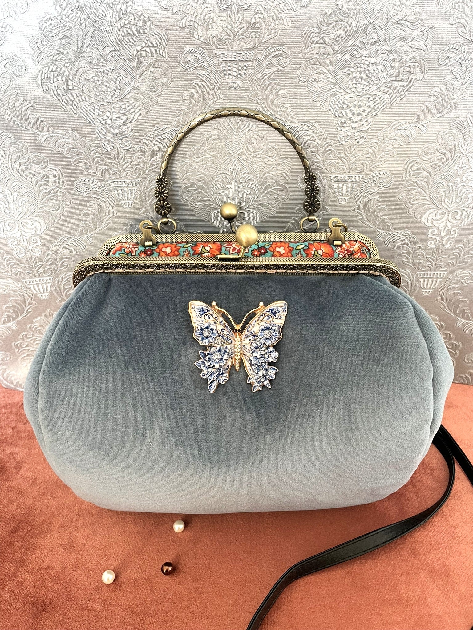 Sac à main rétro en velours bleu azur avec un papillon orné de motifs floraux bleus et blancs.