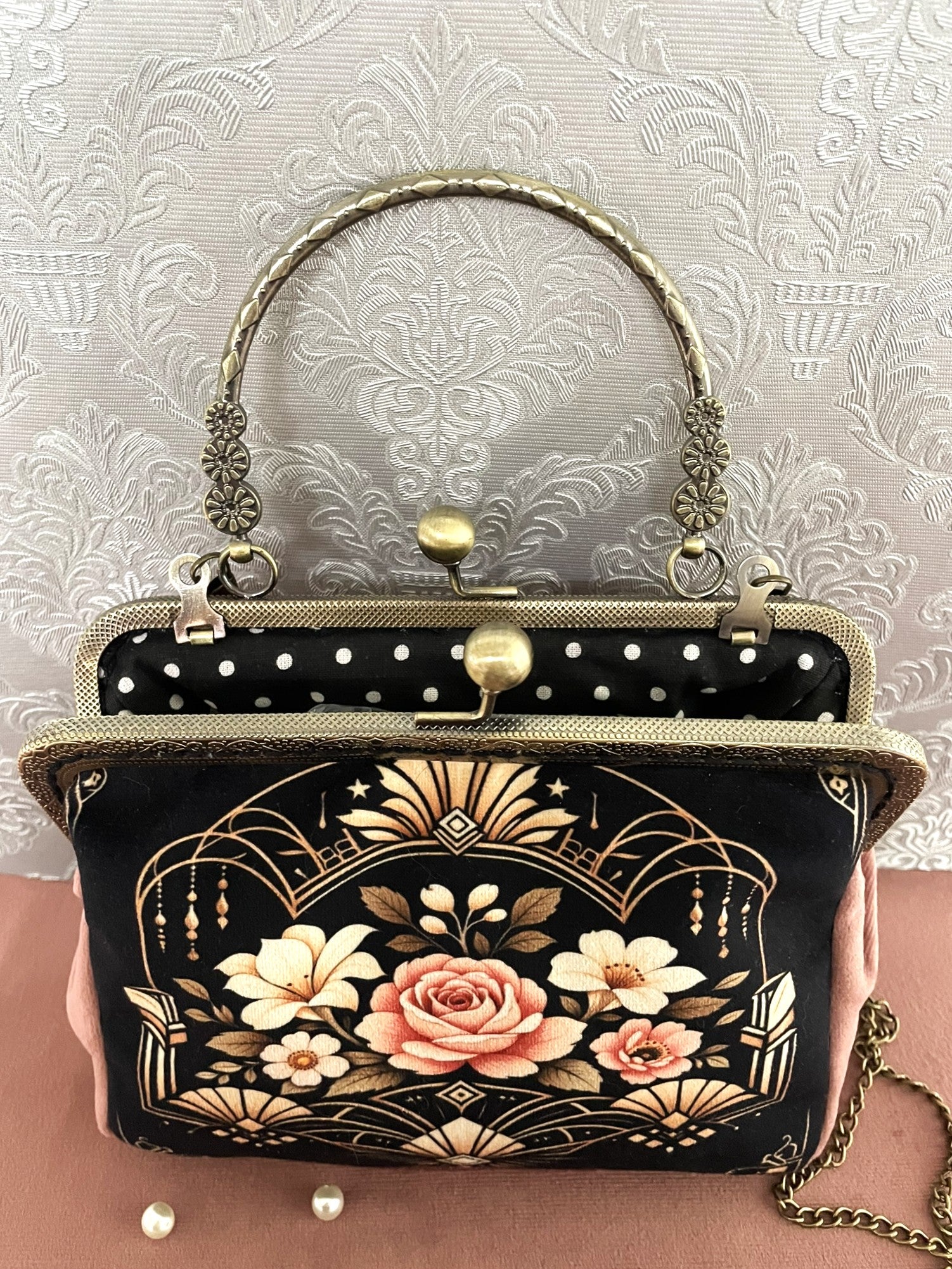 Sac à main vintage ouvert montrant une doublure noire à pois blancs, fermoir clic-clac rétro et anse métallique ciselée.