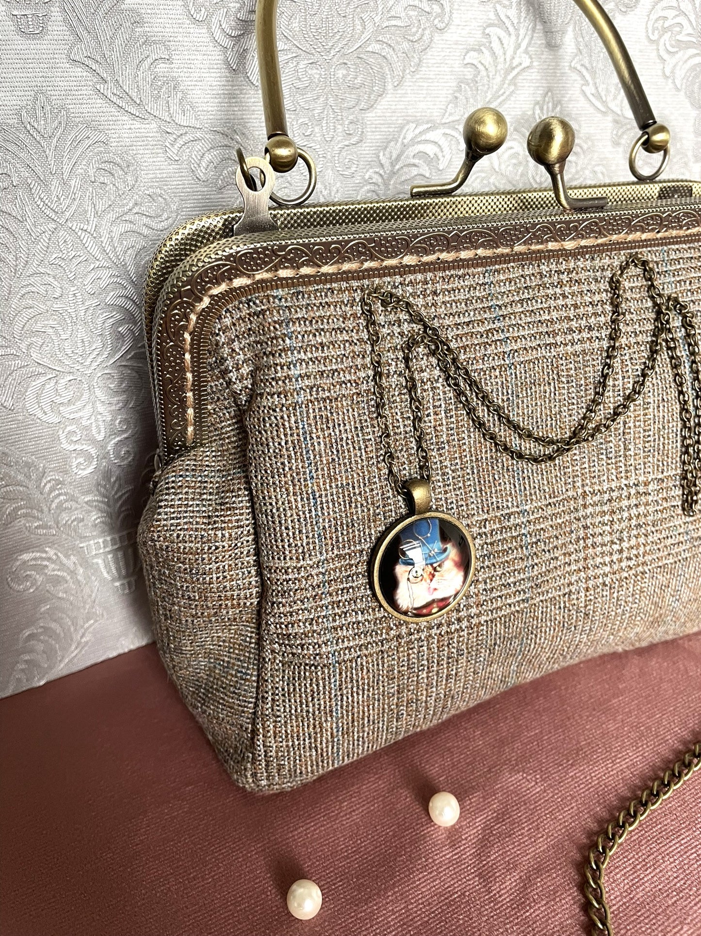 Vue d'un sac rétro en tweed marron à carreaux avec chaîne et pendentif chat gentleman de style dandy rétro.