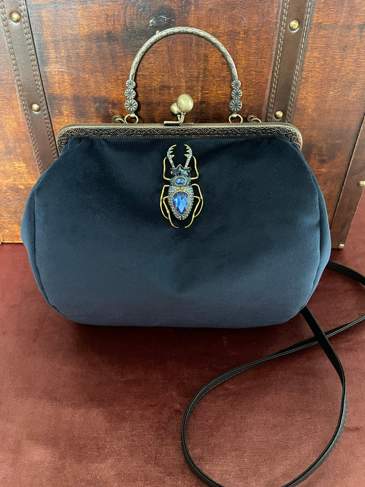 Vue de profil du sac scarabée en velours bleu nuit et anse rigide ciselée.
