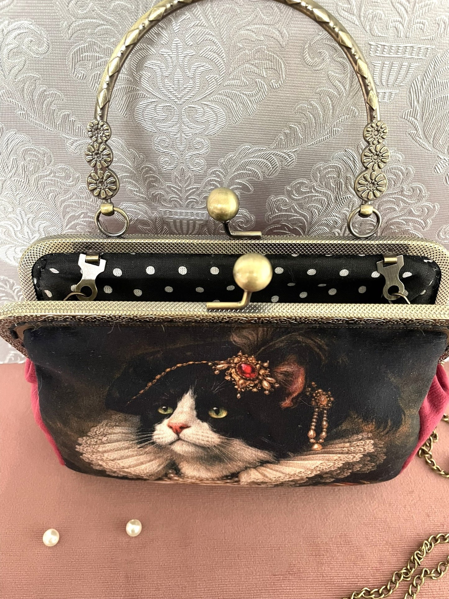 Intérieur ouvert du sac chat baroque montrant une doublure noire à pois blancs et une armature rétro métallique  travaillée.