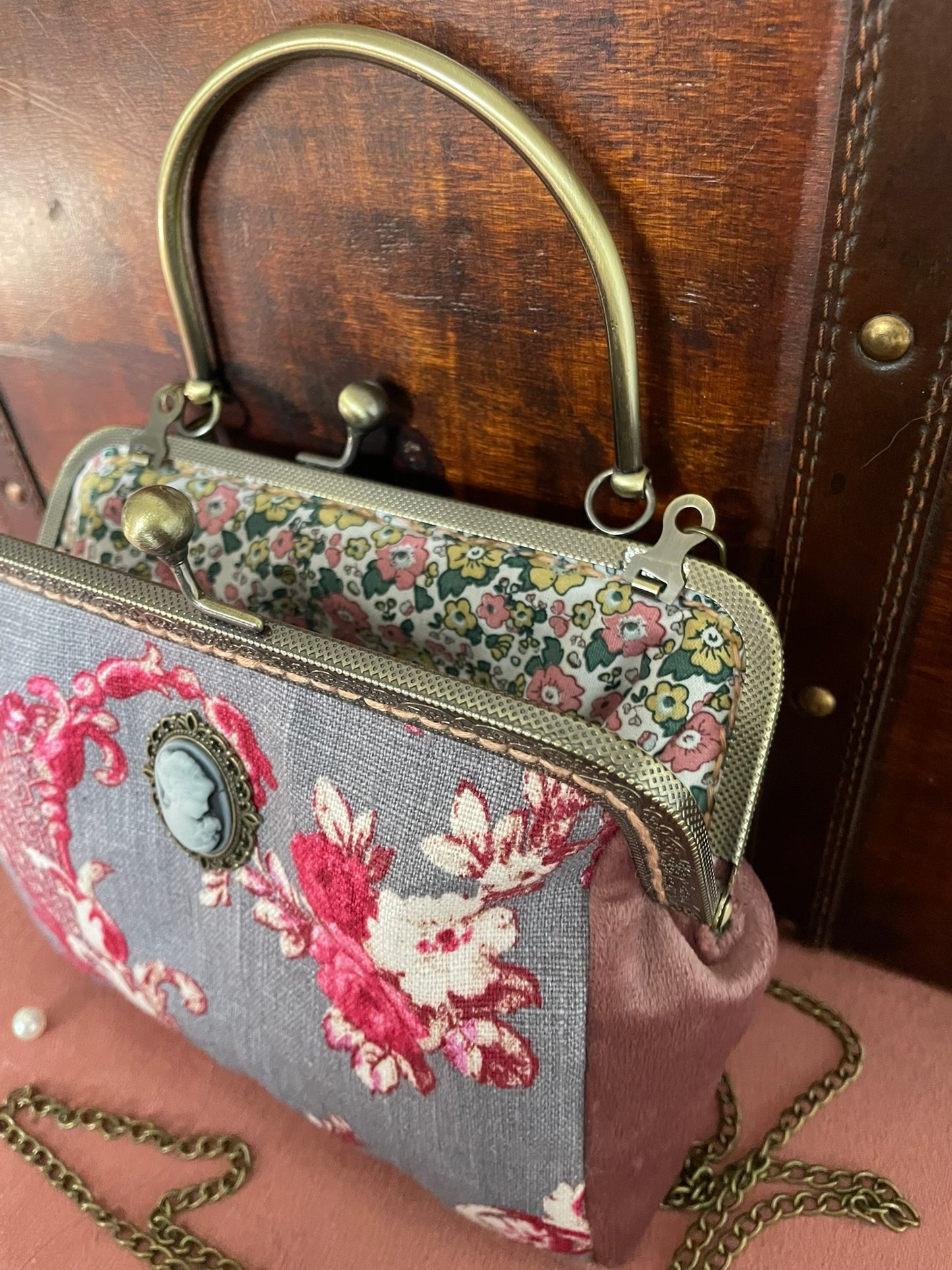 Mise en scène du sac Toile de Jouy devant une malle vintage avec perles décoratives.