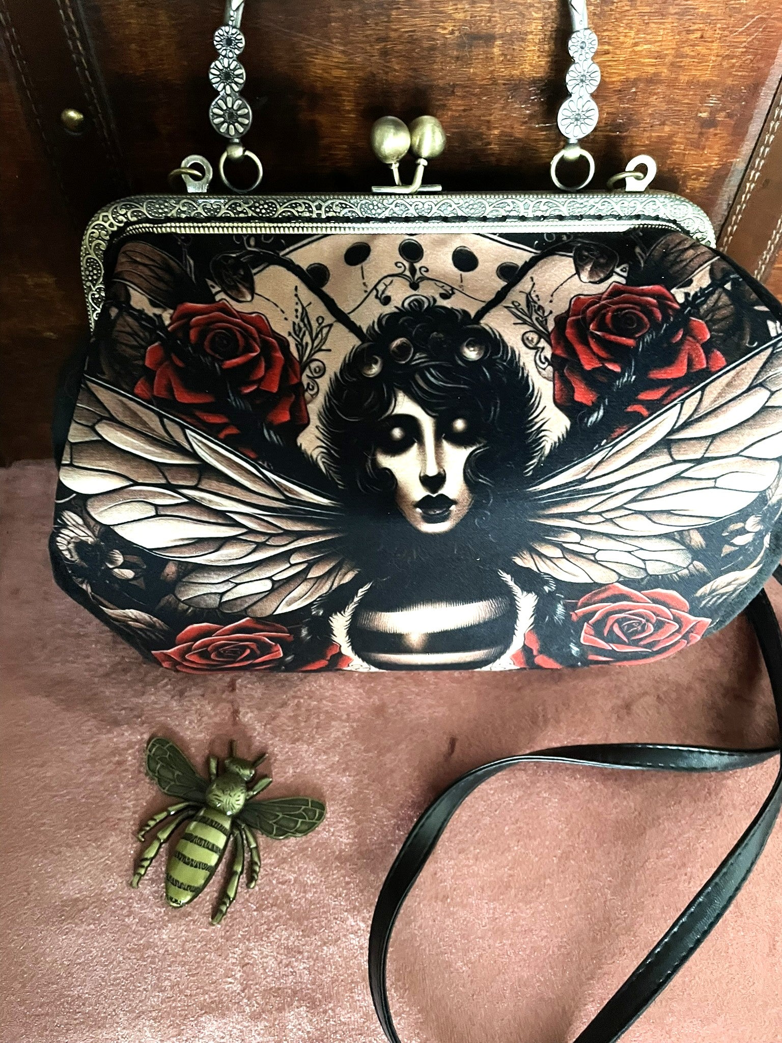Sac à main rétro avec illustration femme-papillon et roses rouges, fermoir métallique effet bronze.